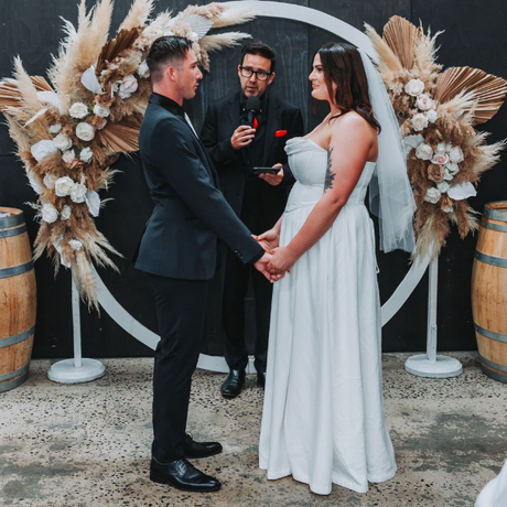 Wedding couple holding hands before officiant under a floral arch