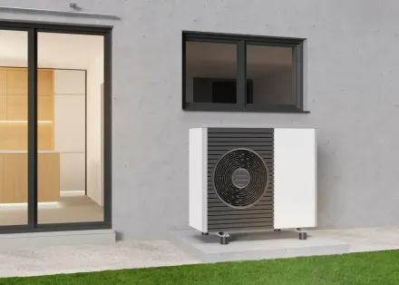 Unità esterna della pompa di calore accanto a una parete e una finestra di una casa moderna, con porte finestre e prato nelle vicinanze.