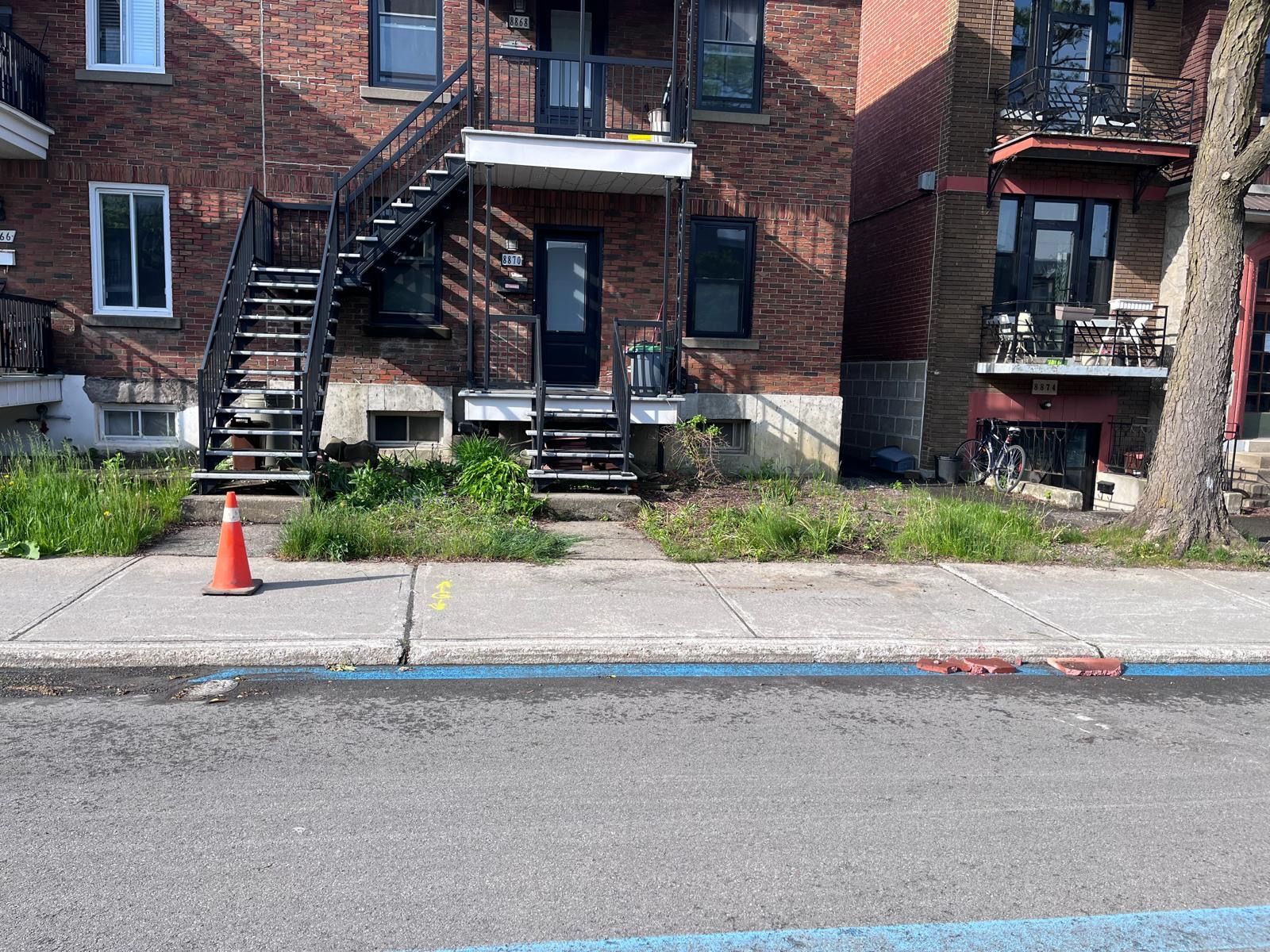 Un bâtiment en briques avec des escaliers et un cône sur le trottoir devant lui.