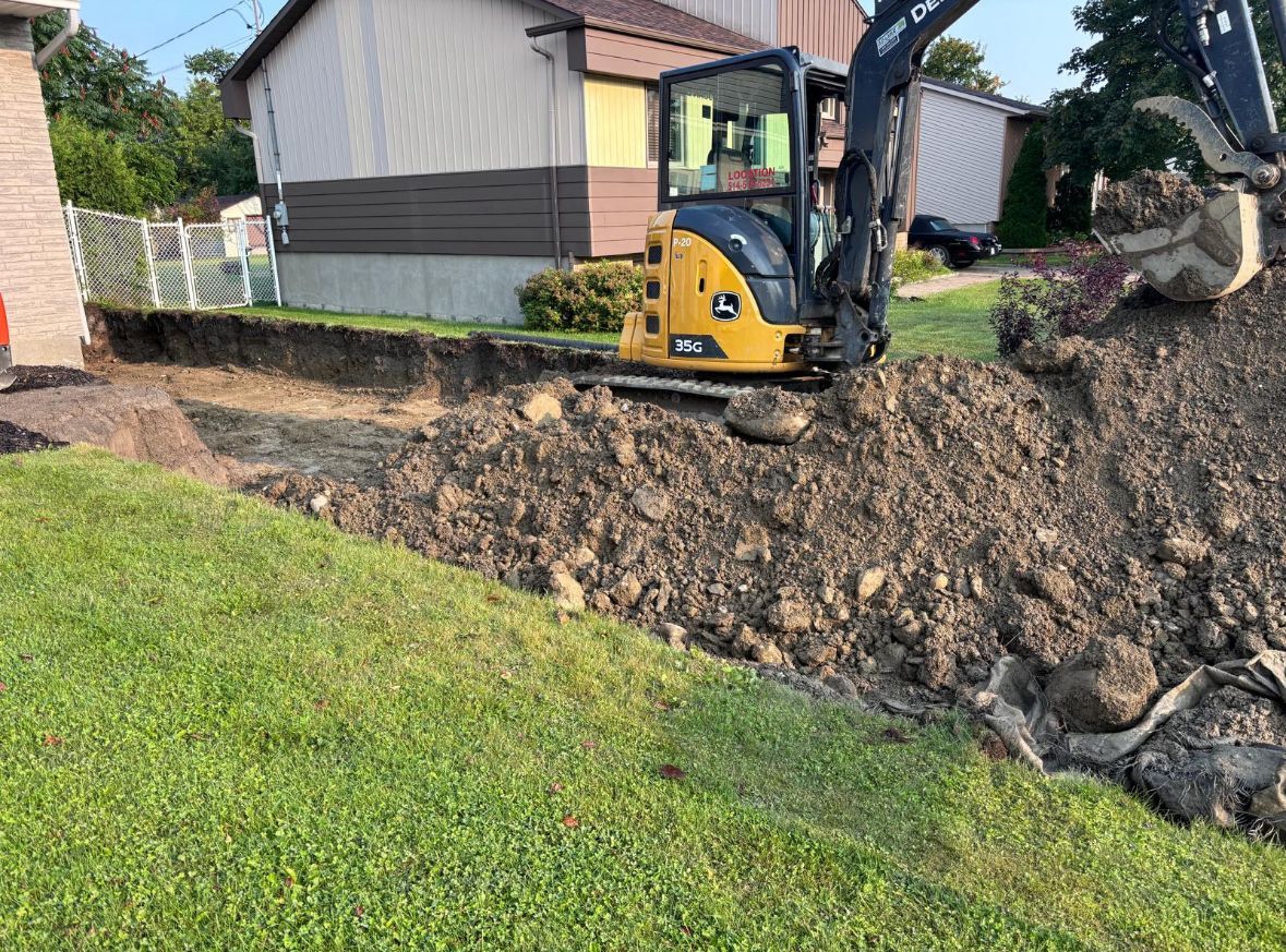 Une petite excavatrice creuse un trou dans le sol devant une maison.