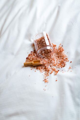 a glass filled with pink salt and a wooden spoon on a white towel.