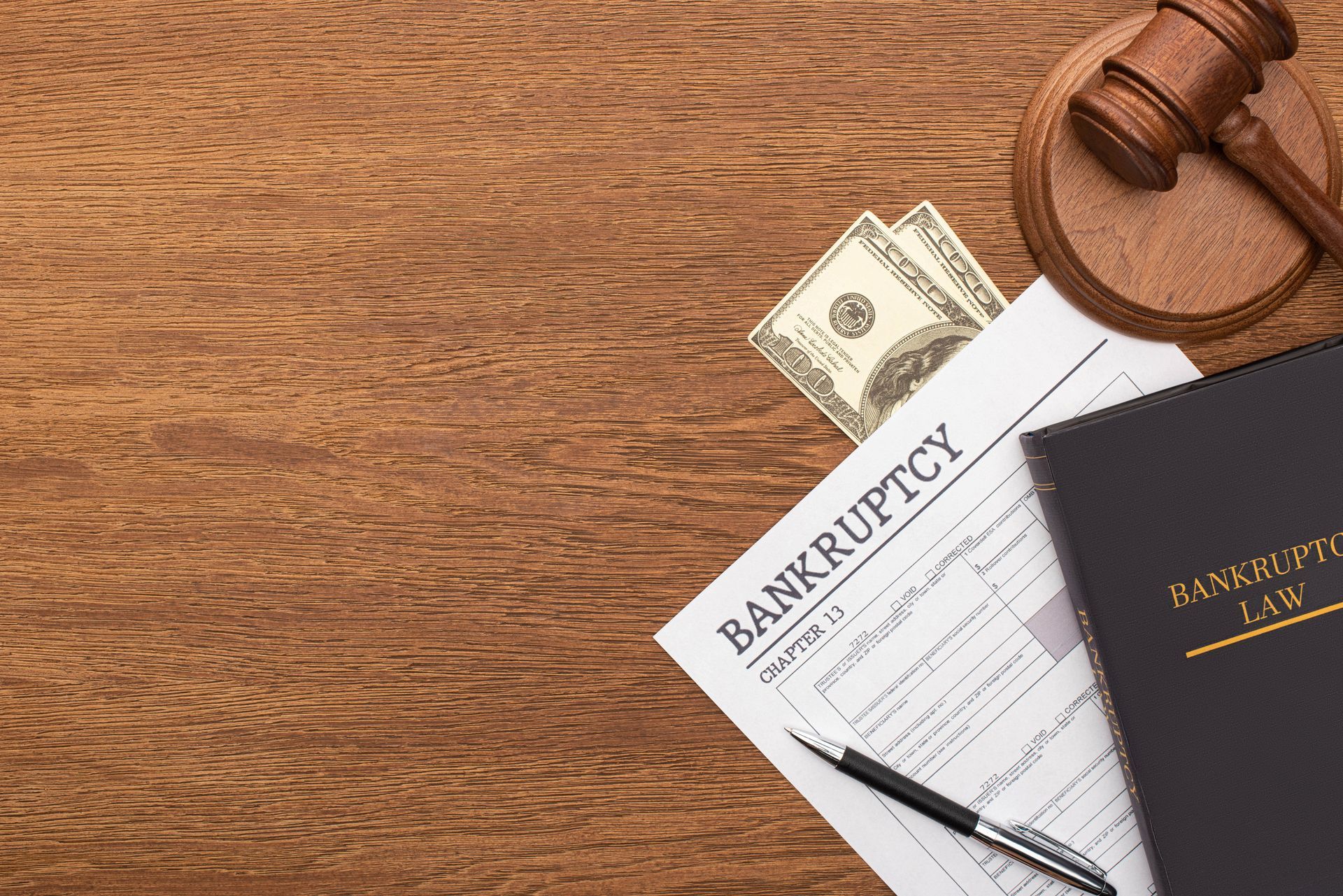 A bankruptcy form , a judge 's gavel , a pen and a book on a wooden table.