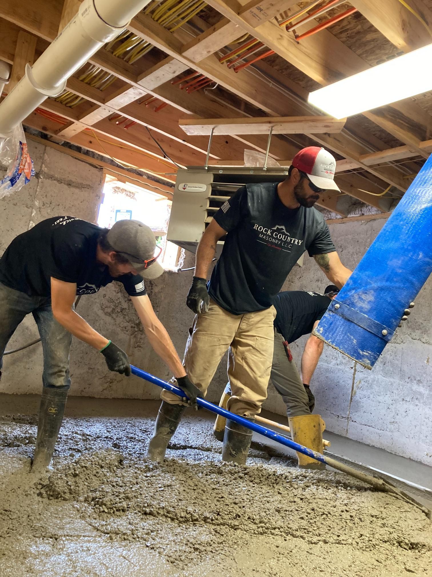 Two men are working on a concrete floor in a basement.