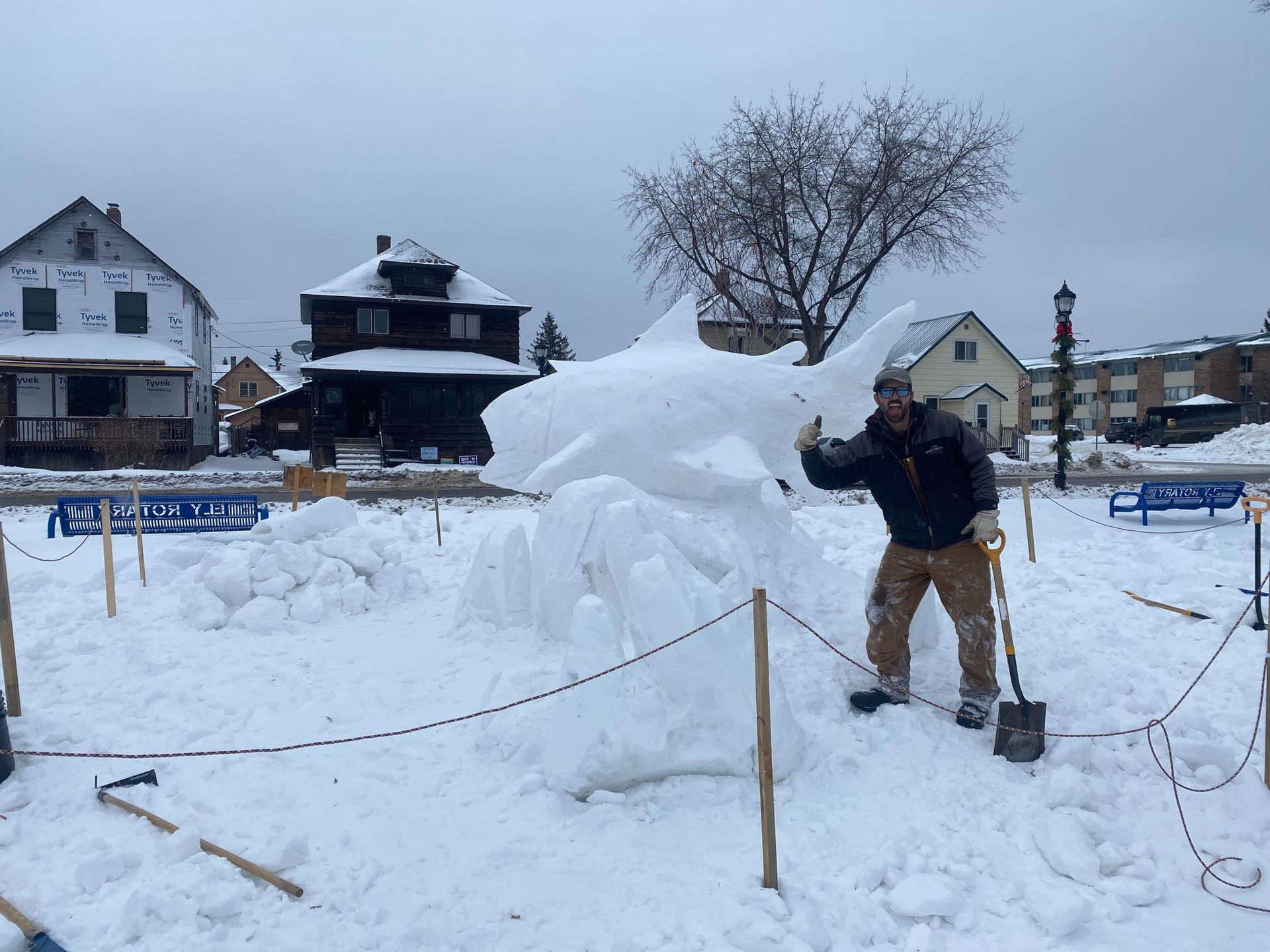 A man is standing in front of a snow sculpture of a shark.