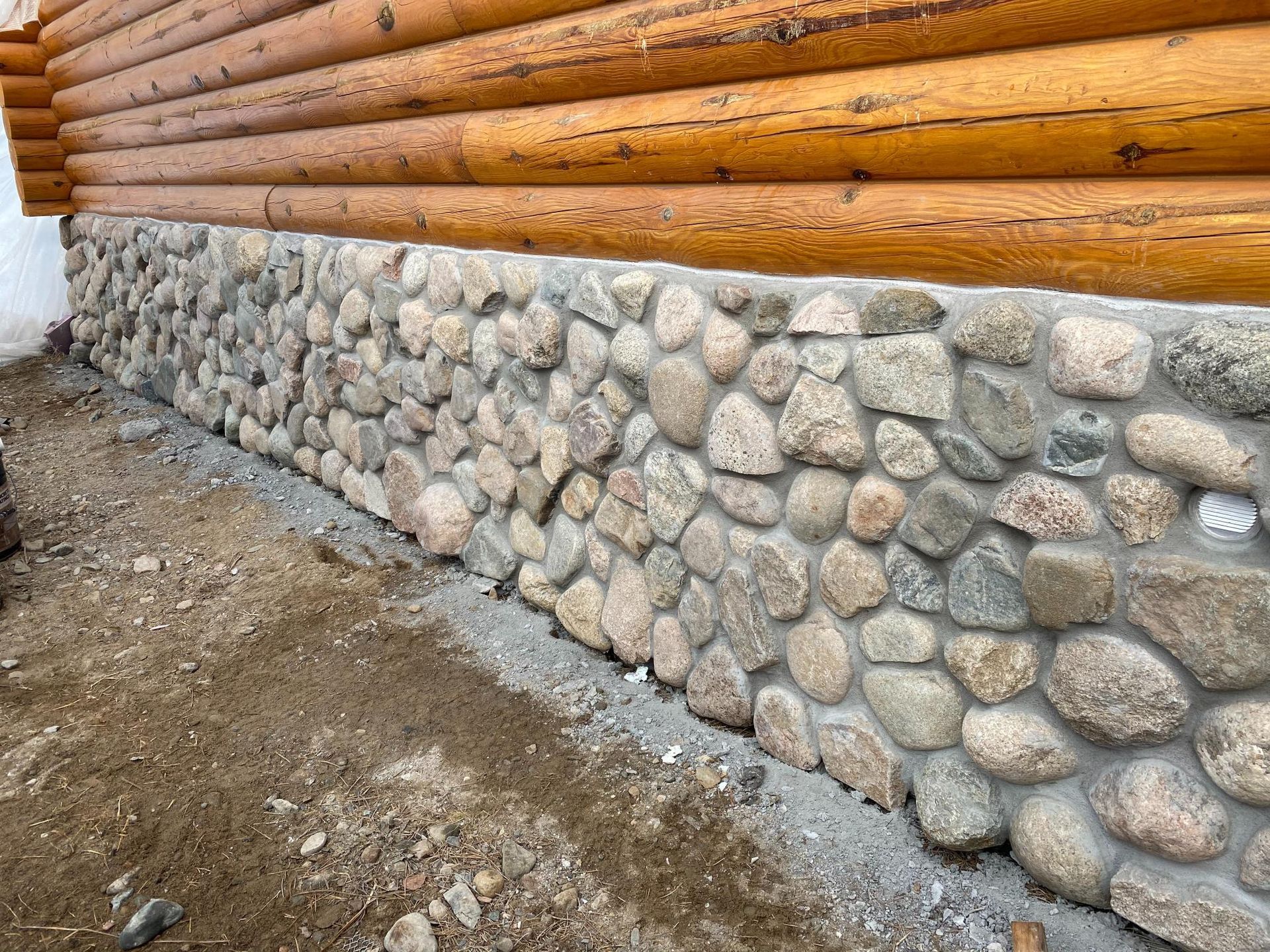 A log cabin with a stone wall on the side of it.