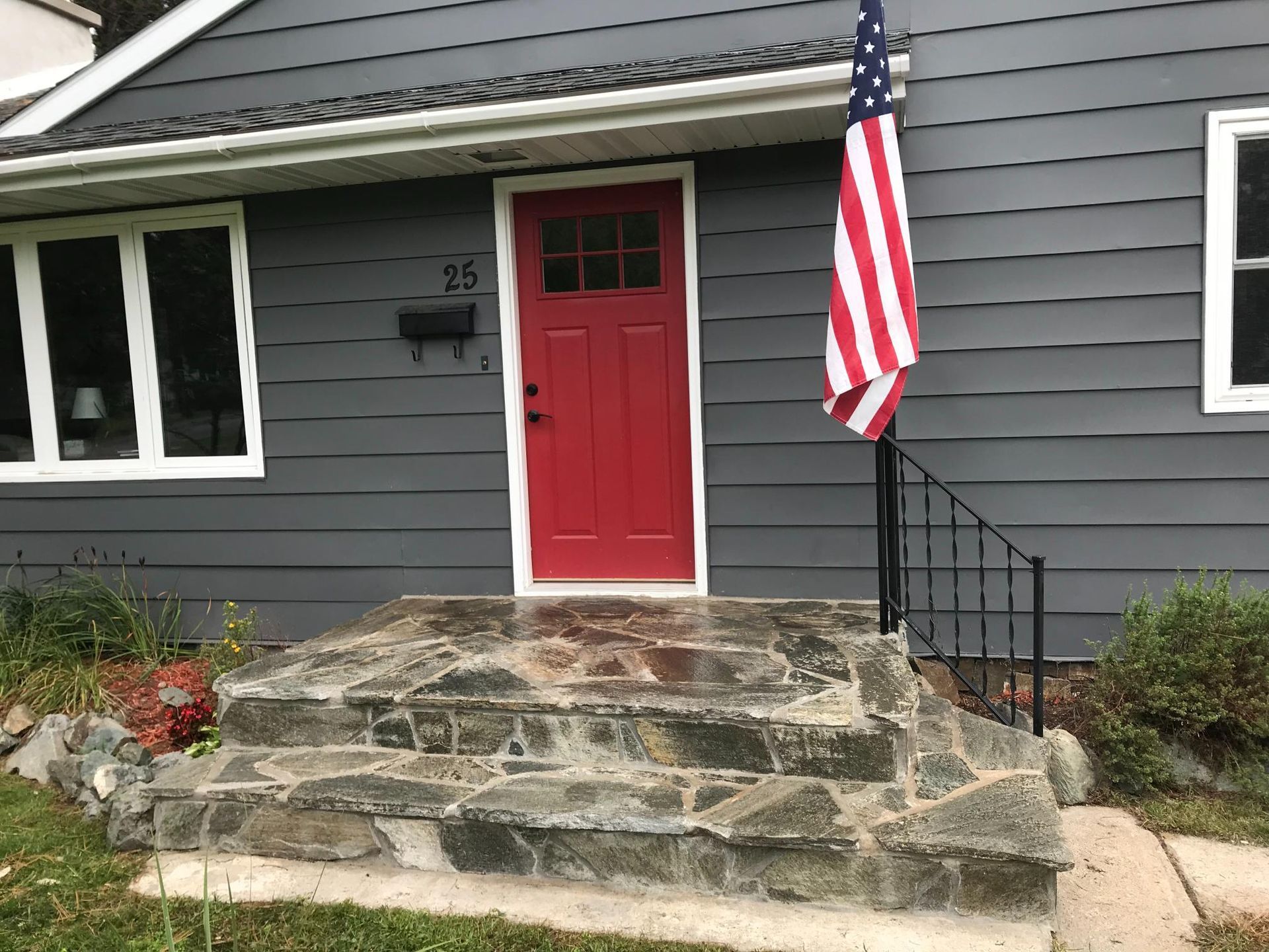 A red door is on the front of a gray house.