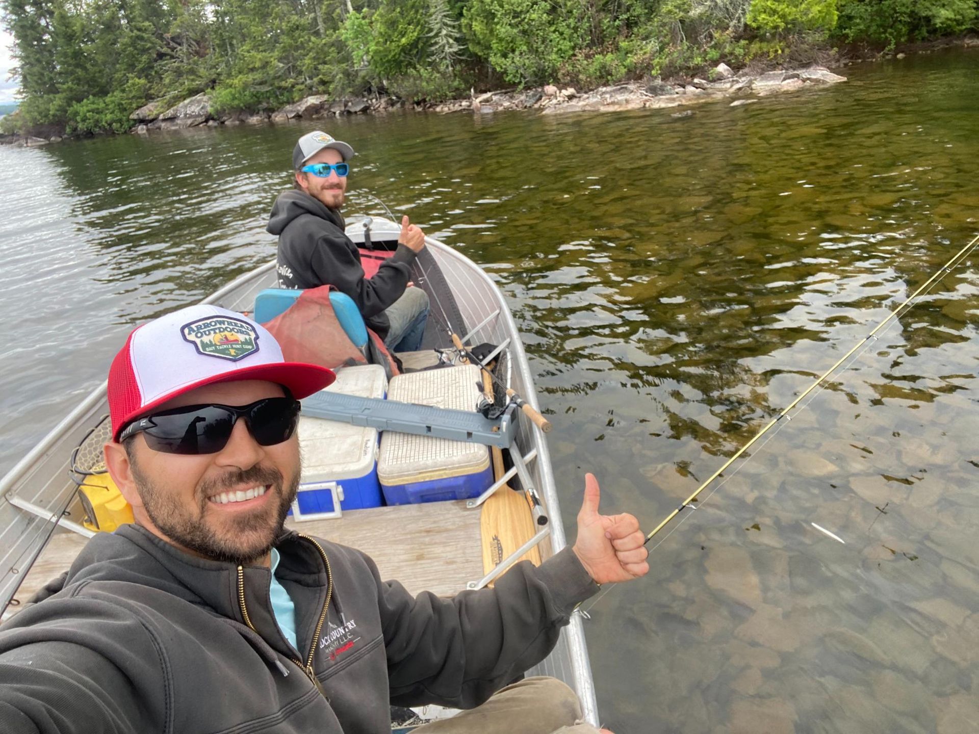 Two men are fishing in a boat on a lake and one of them is giving a thumbs up.