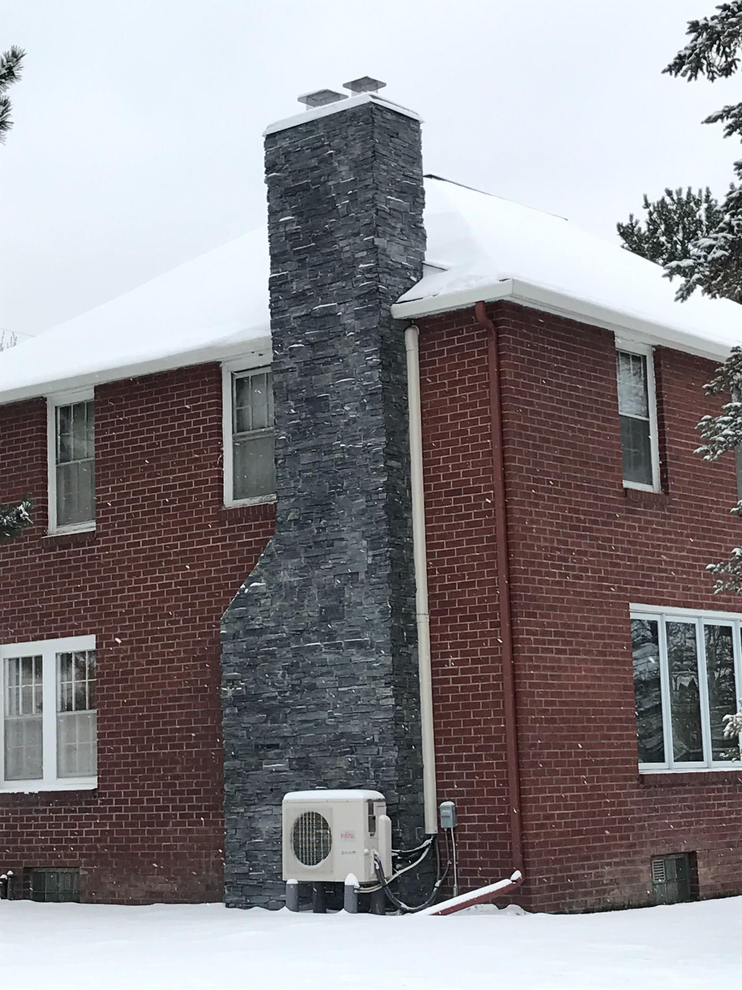 A red brick house with a large chimney in the snow.