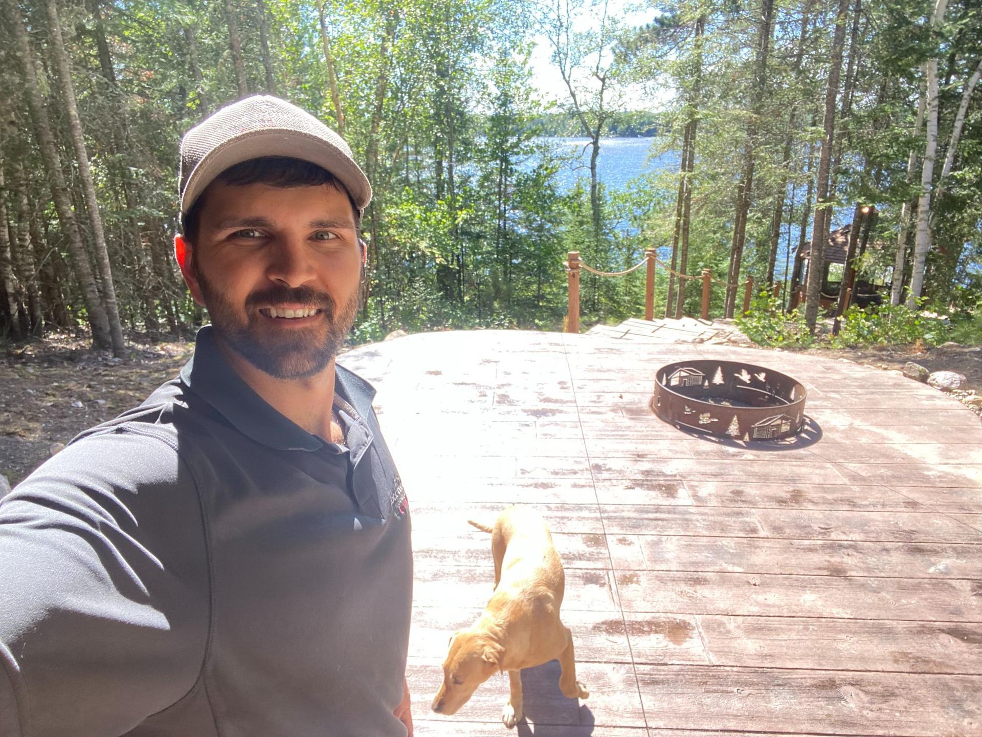 A man is taking a selfie with a dog on a wooden deck.