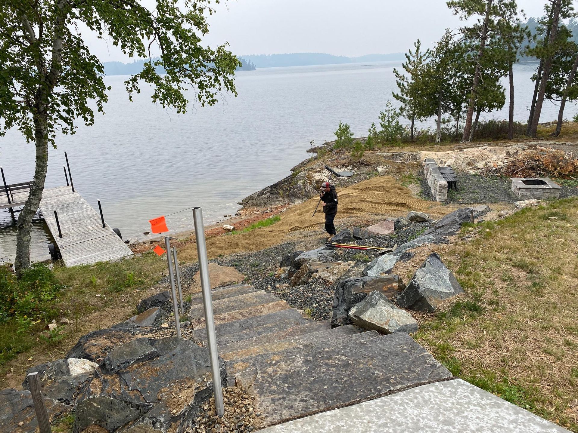 A man is standing on the shore of a lake next to a dock.
