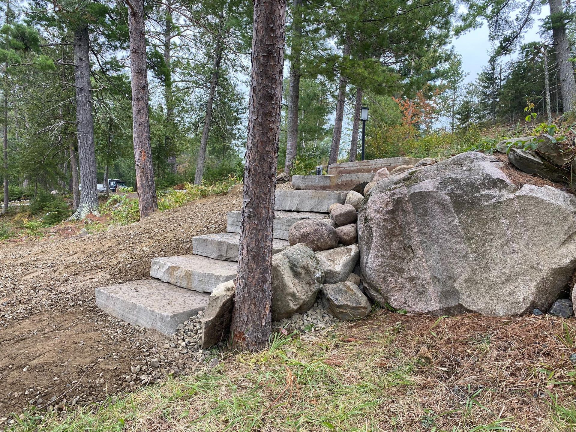 A set of stone stairs leading up to a rock wall surrounded by trees.