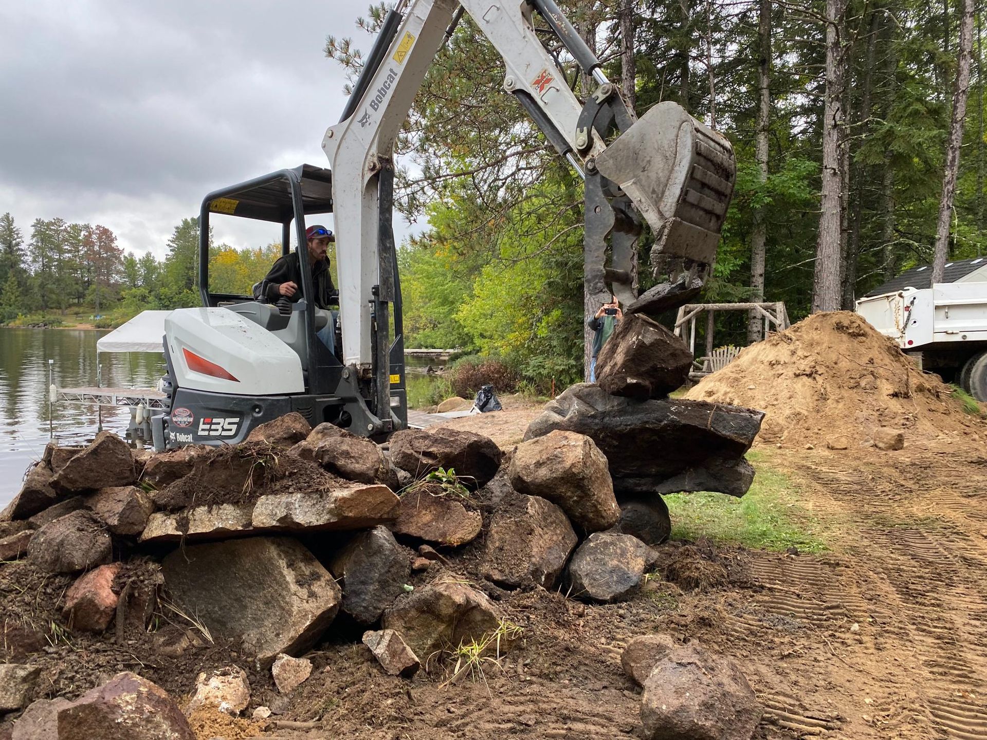 A man is driving an excavator over a pile of rocks.
