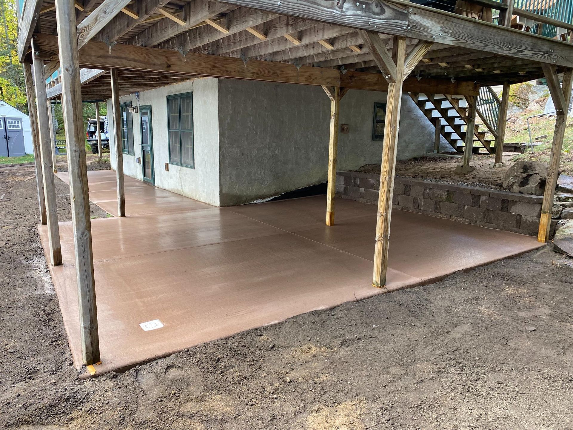 A concrete patio under a wooden deck next to a house.