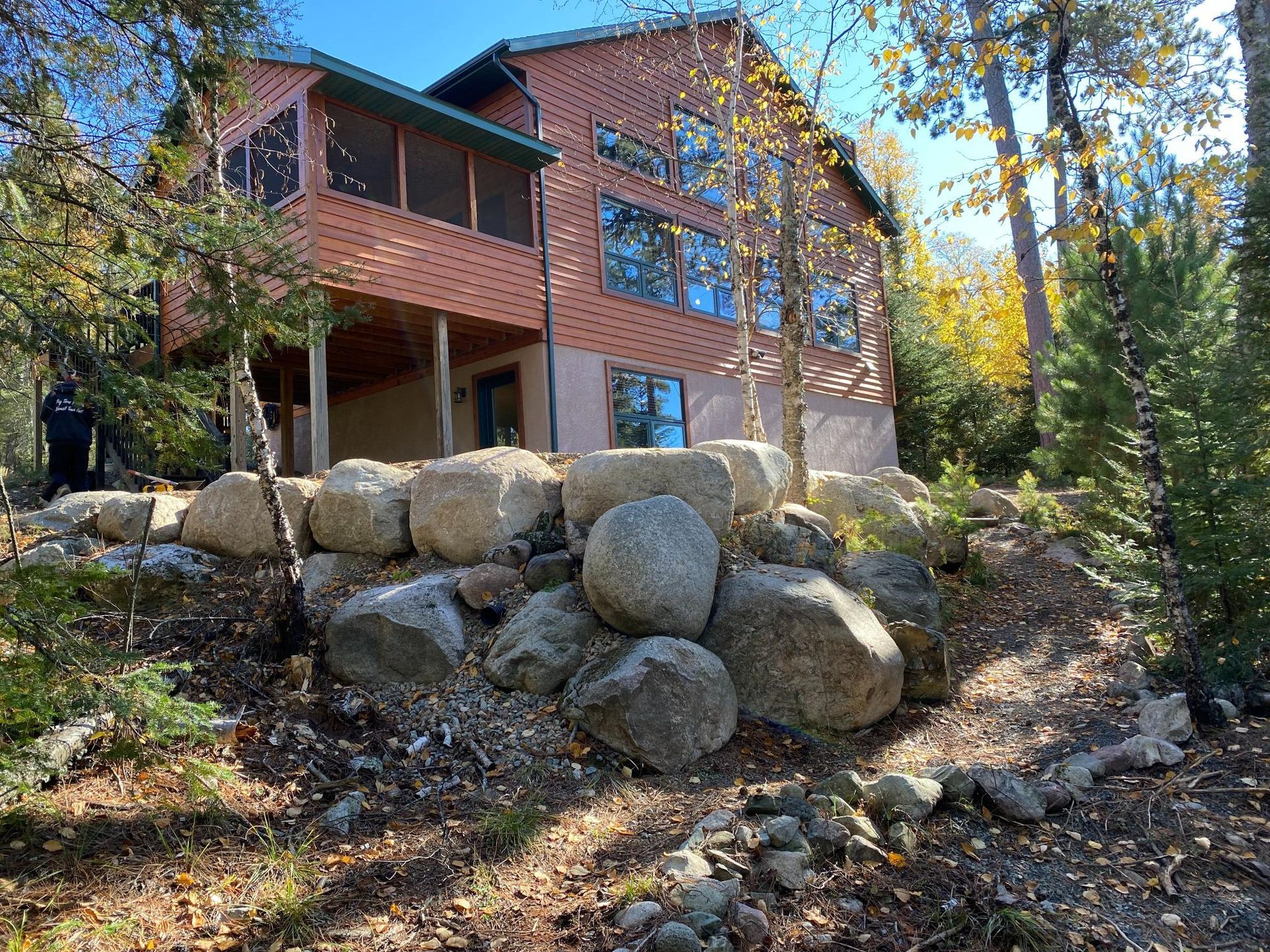 A large house with a screened in porch is surrounded by trees and rocks.