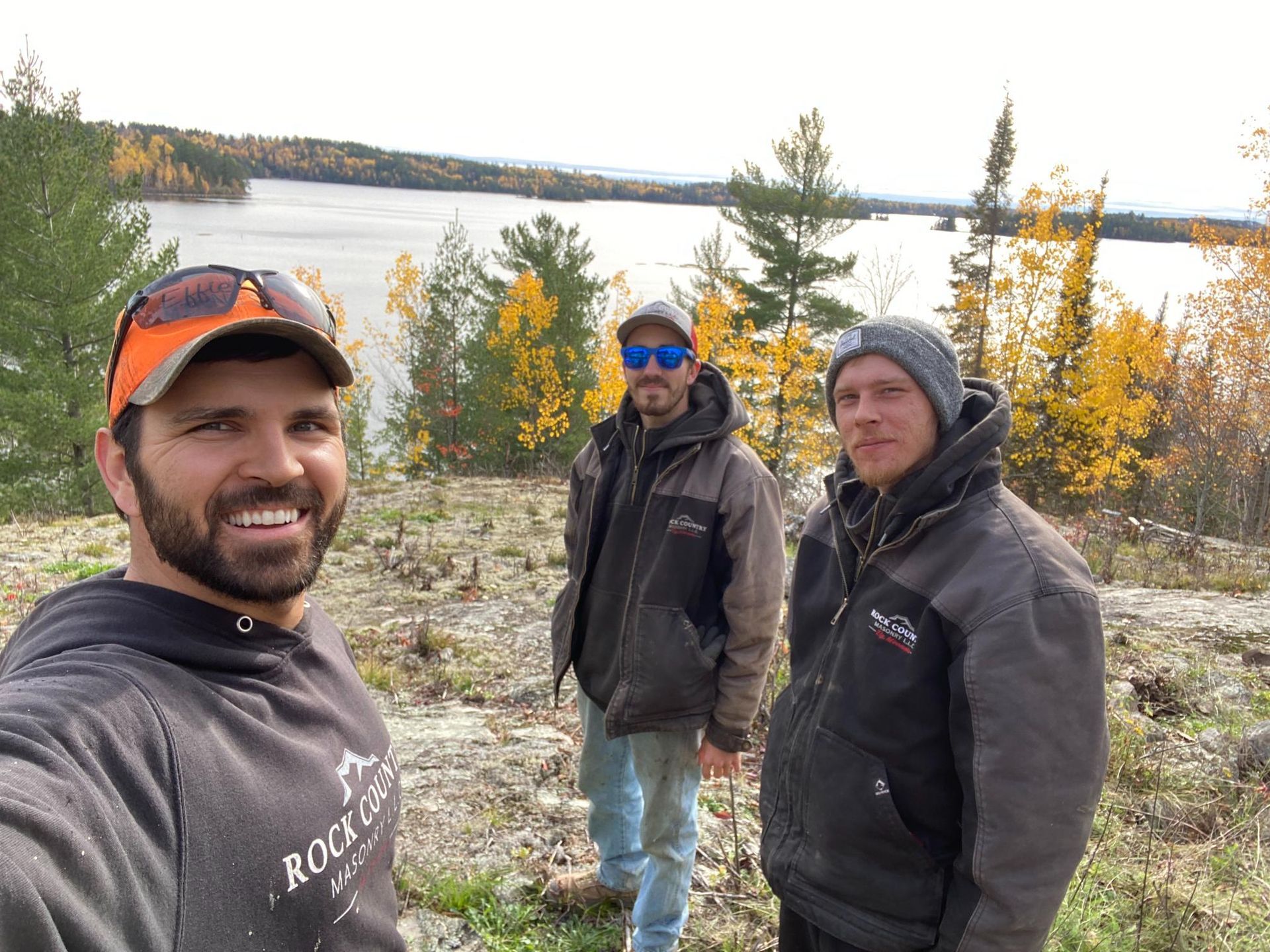 Three men are standing next to each other in front of a lake.