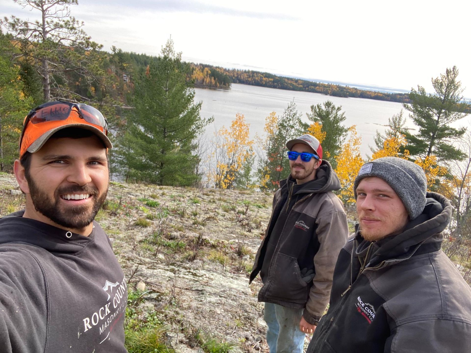Three men are standing on a rocky cliff overlooking a lake.