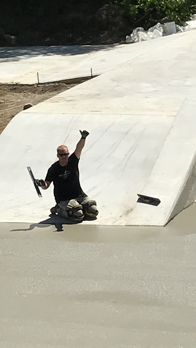 A man is laying on a skateboard on a ramp while holding a trowel.