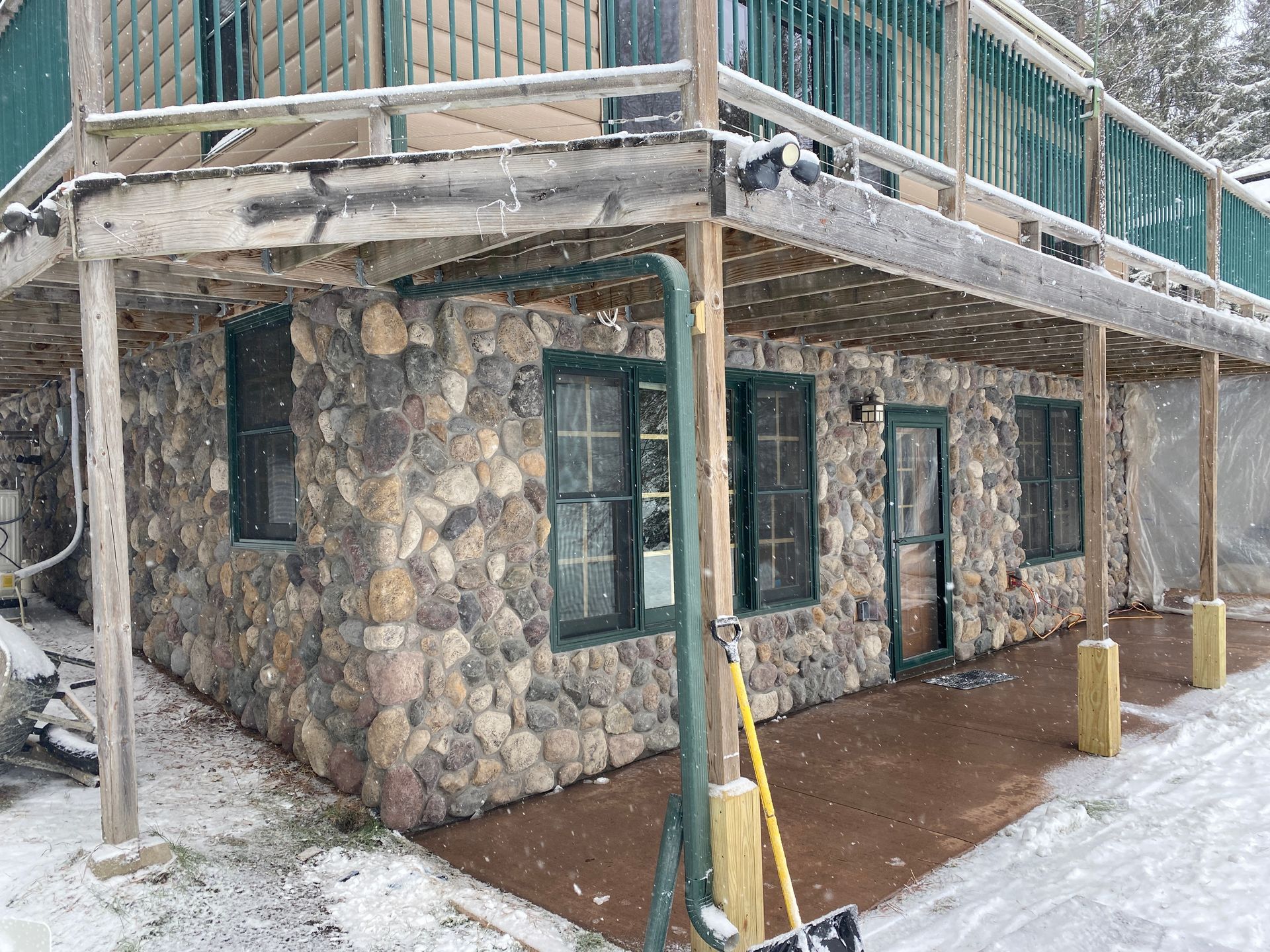 A stone building with a wooden deck and a snow shovel in front of it.