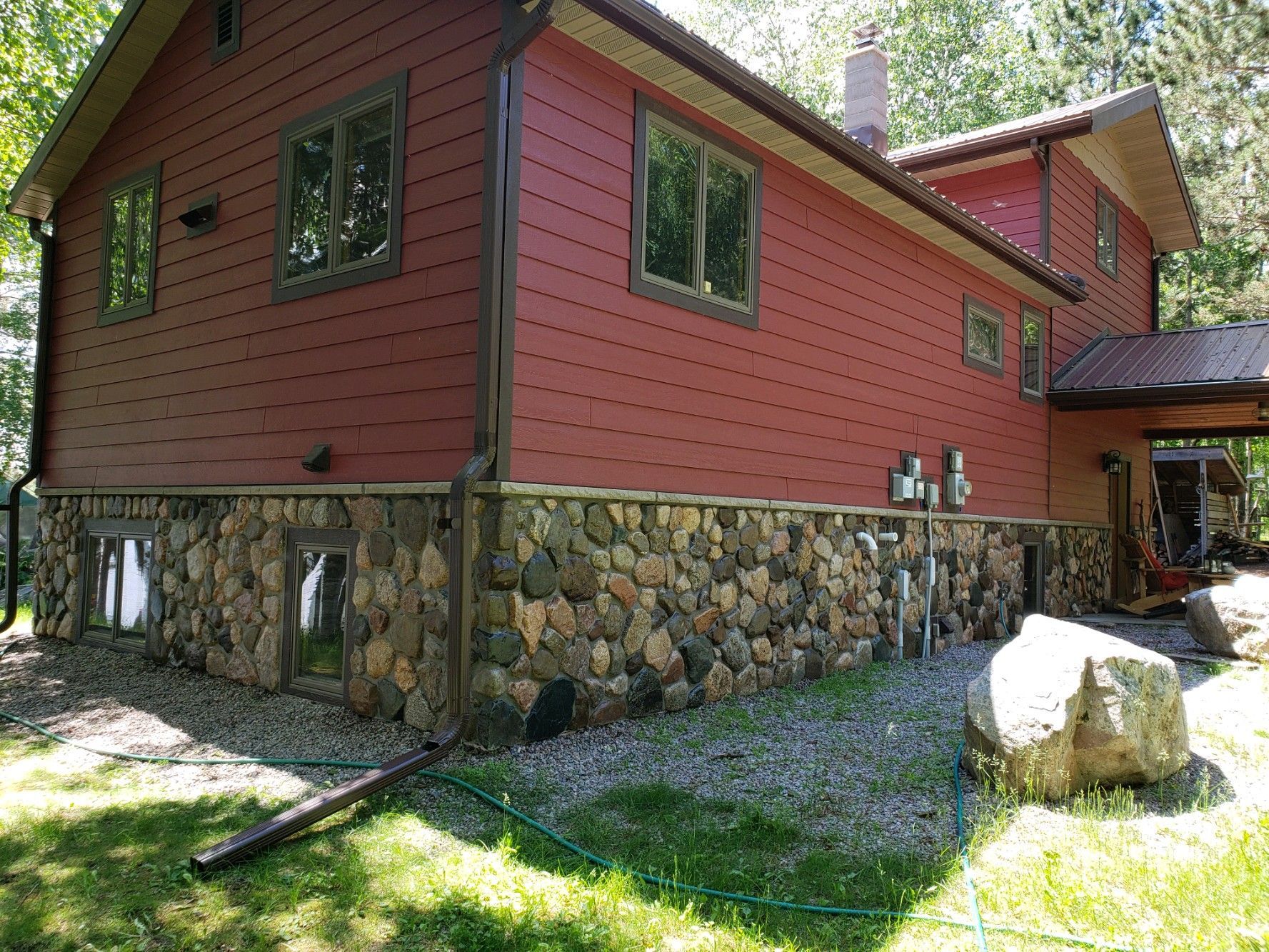 A red house with a stone foundation and a hose in front of it.