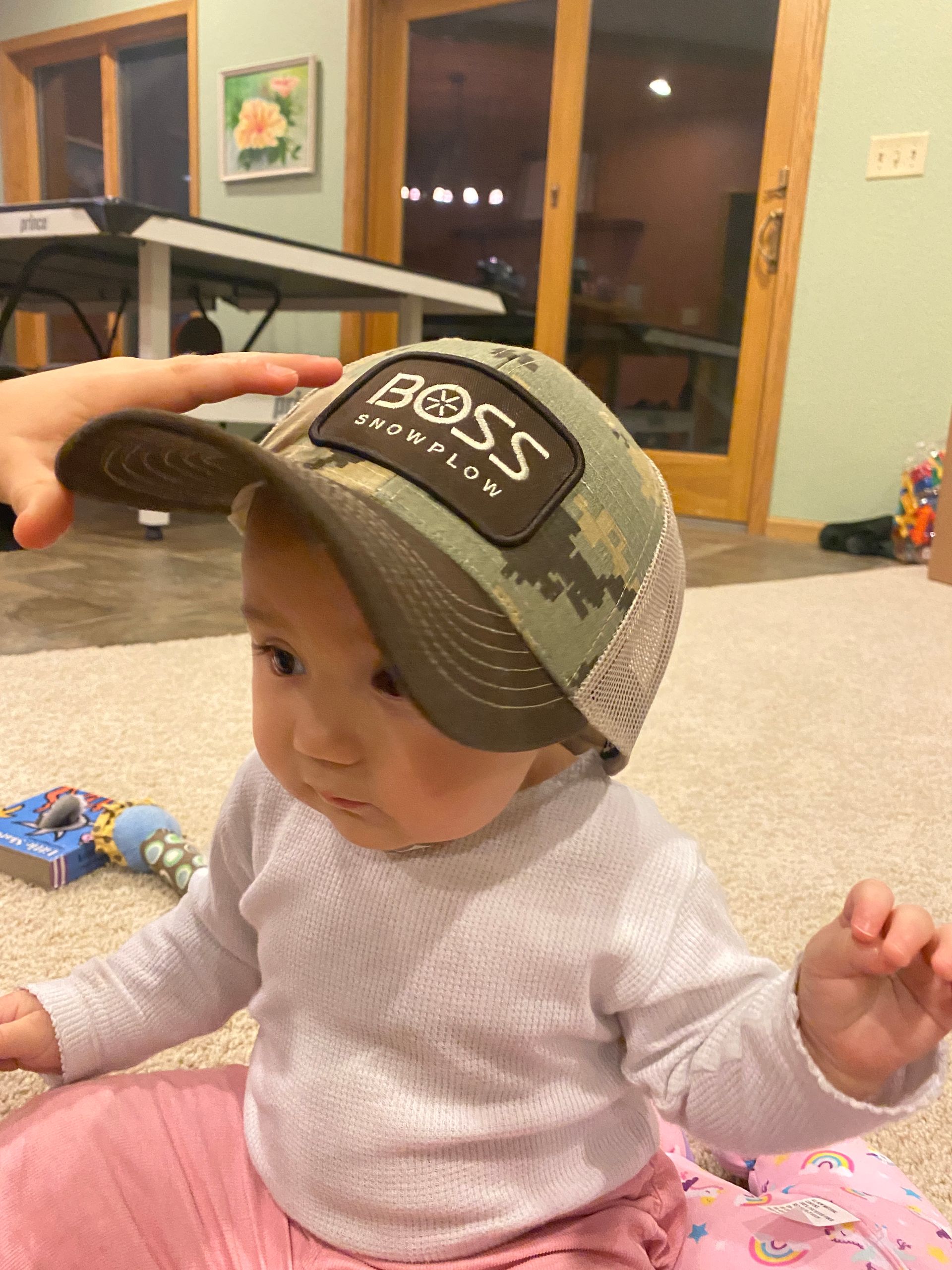 A baby wearing a boss hat is sitting on the floor.