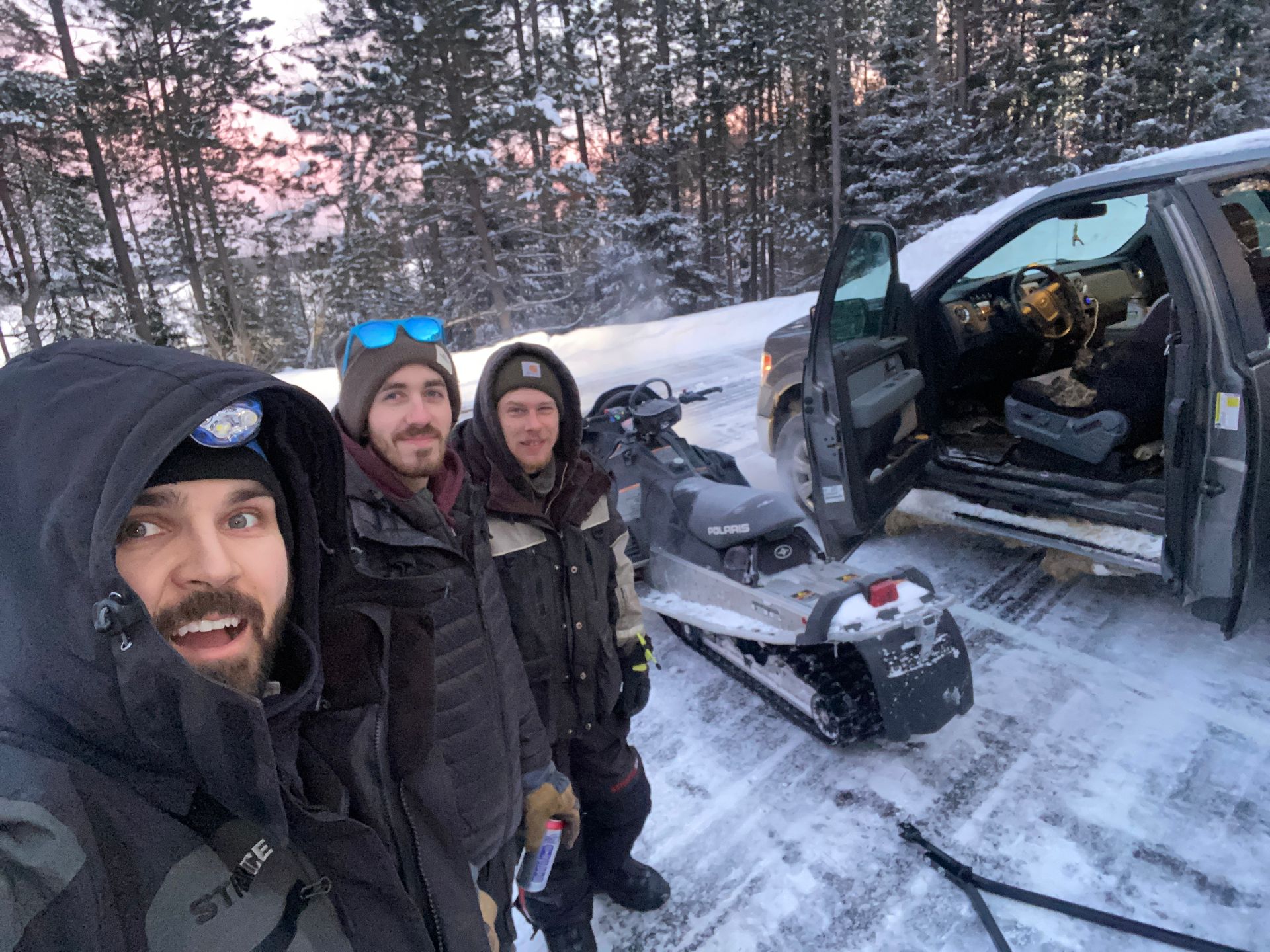 A group of men are standing next to a snowmobile in the snow.