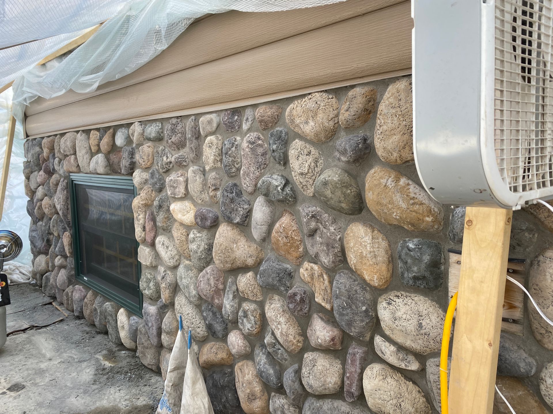 A fan is sitting on a wooden post next to a stone wall.