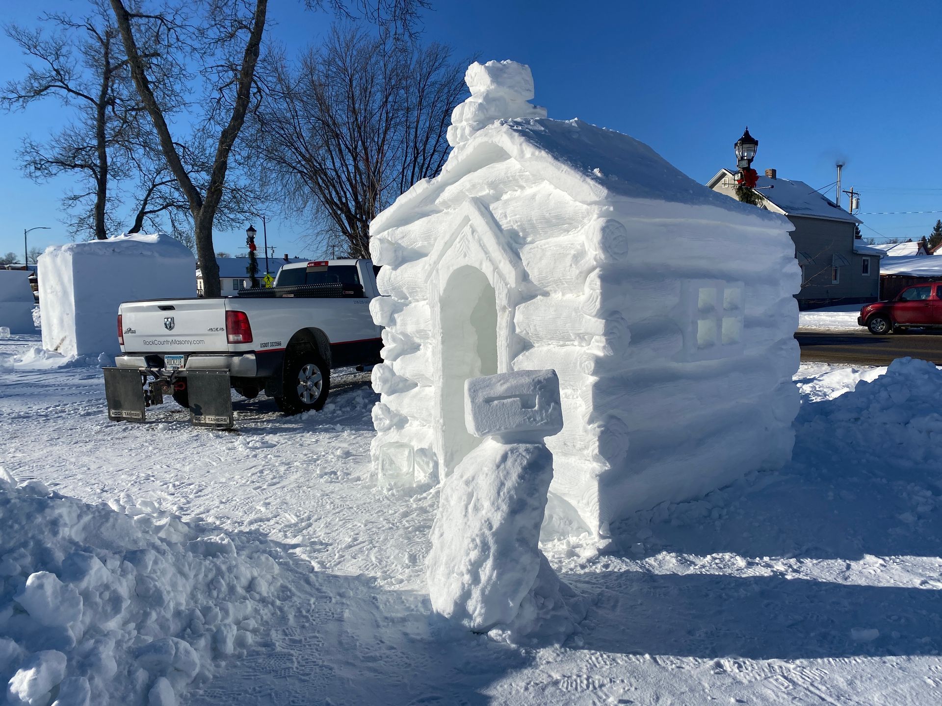 A log cabin made out of snow is sitting in the snow next to a truck.