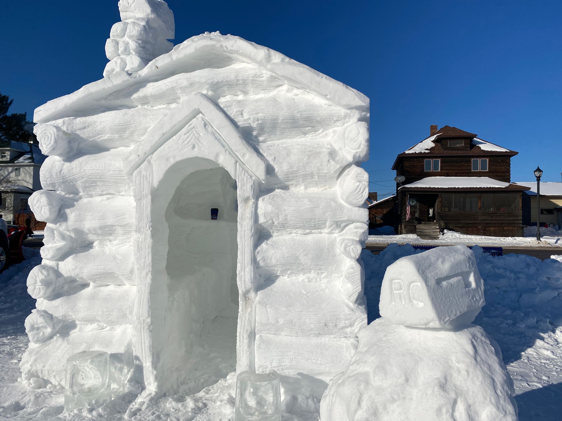 A snow sculpture of a log cabin and a snowman