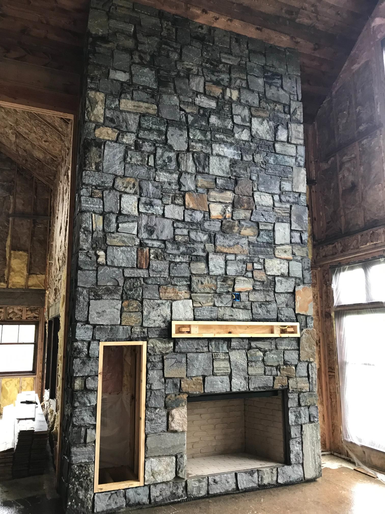A large stone fireplace in a living room with a wooden ceiling.