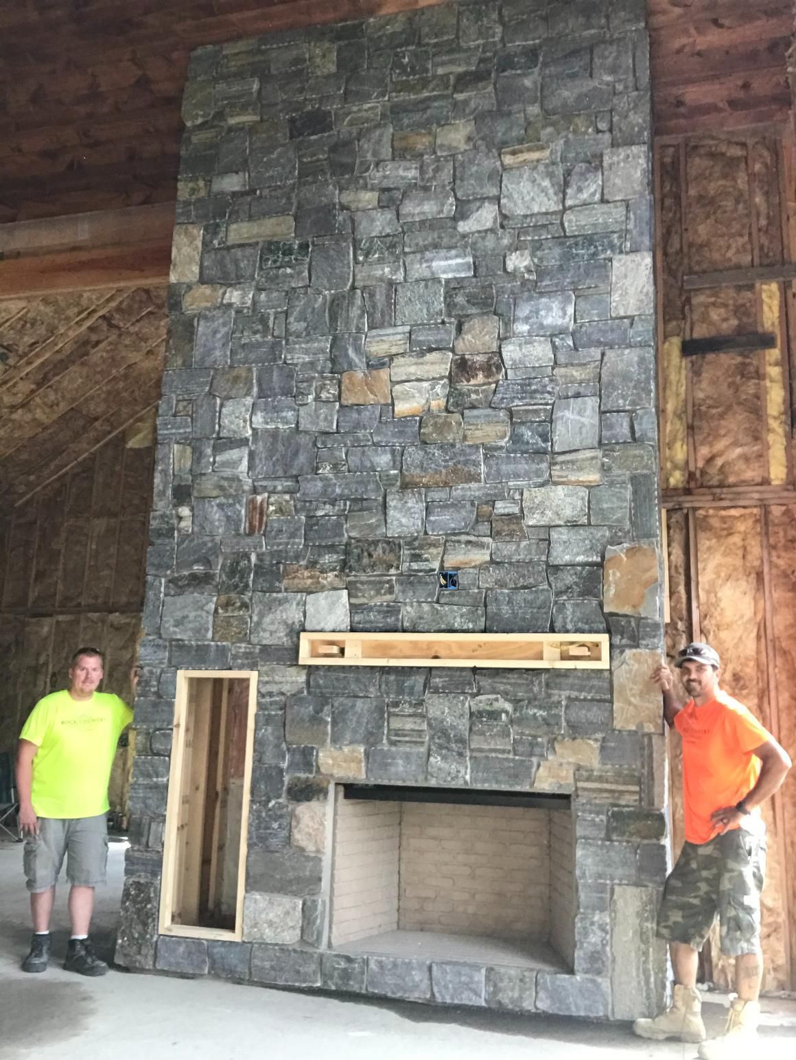 Two men are standing in front of a large stone fireplace.