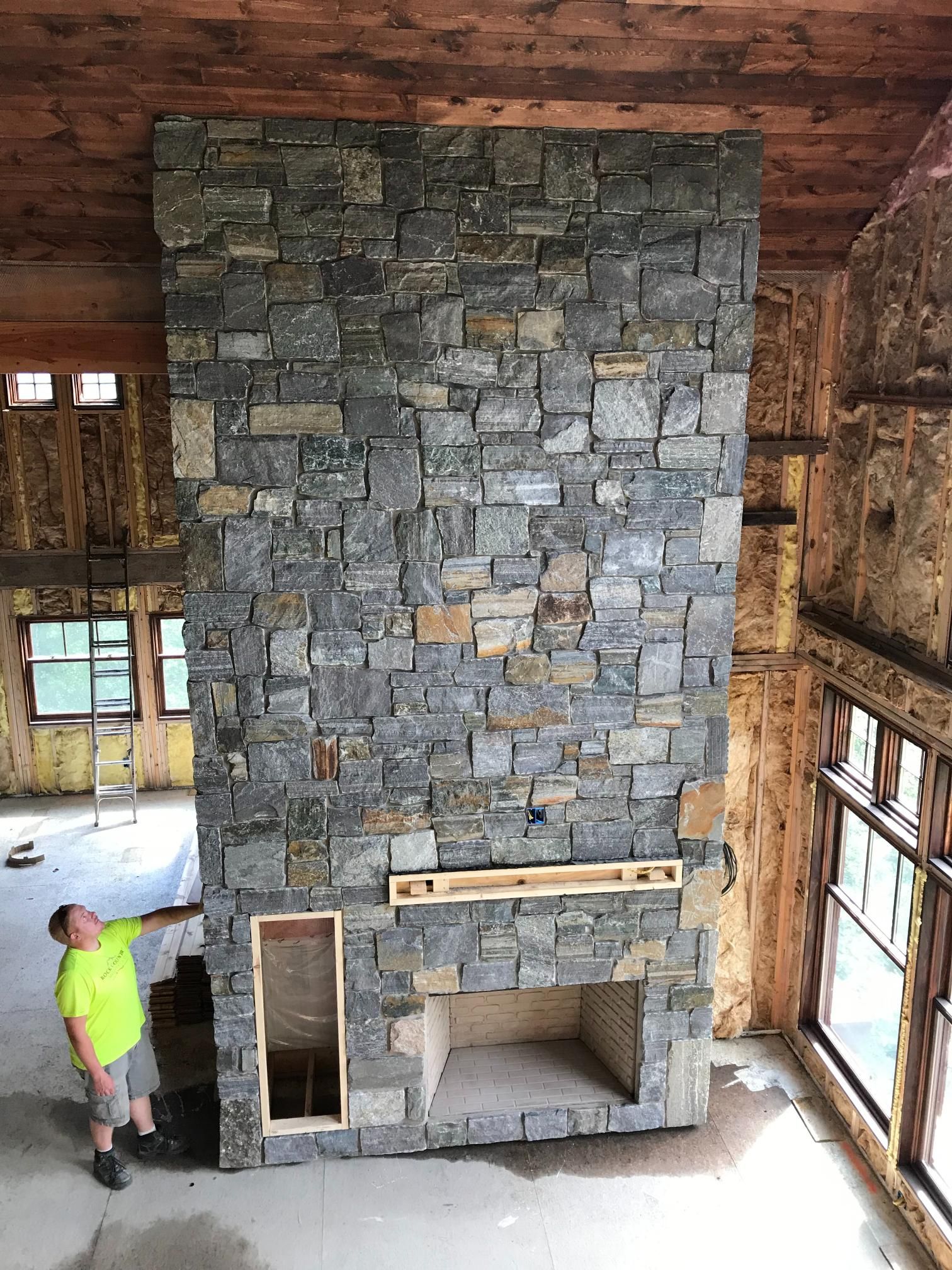 A man is standing in front of a large stone fireplace.