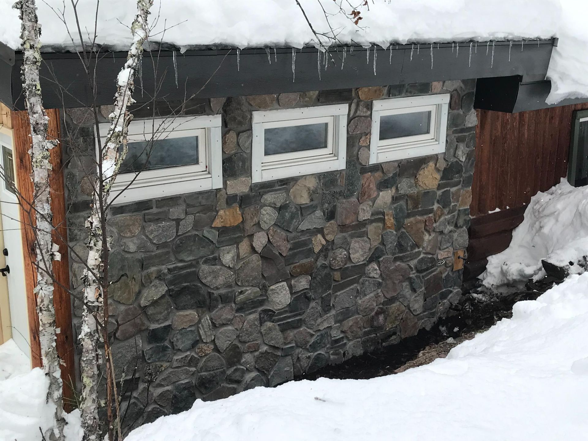 A stone wall with three windows on it is covered in snow