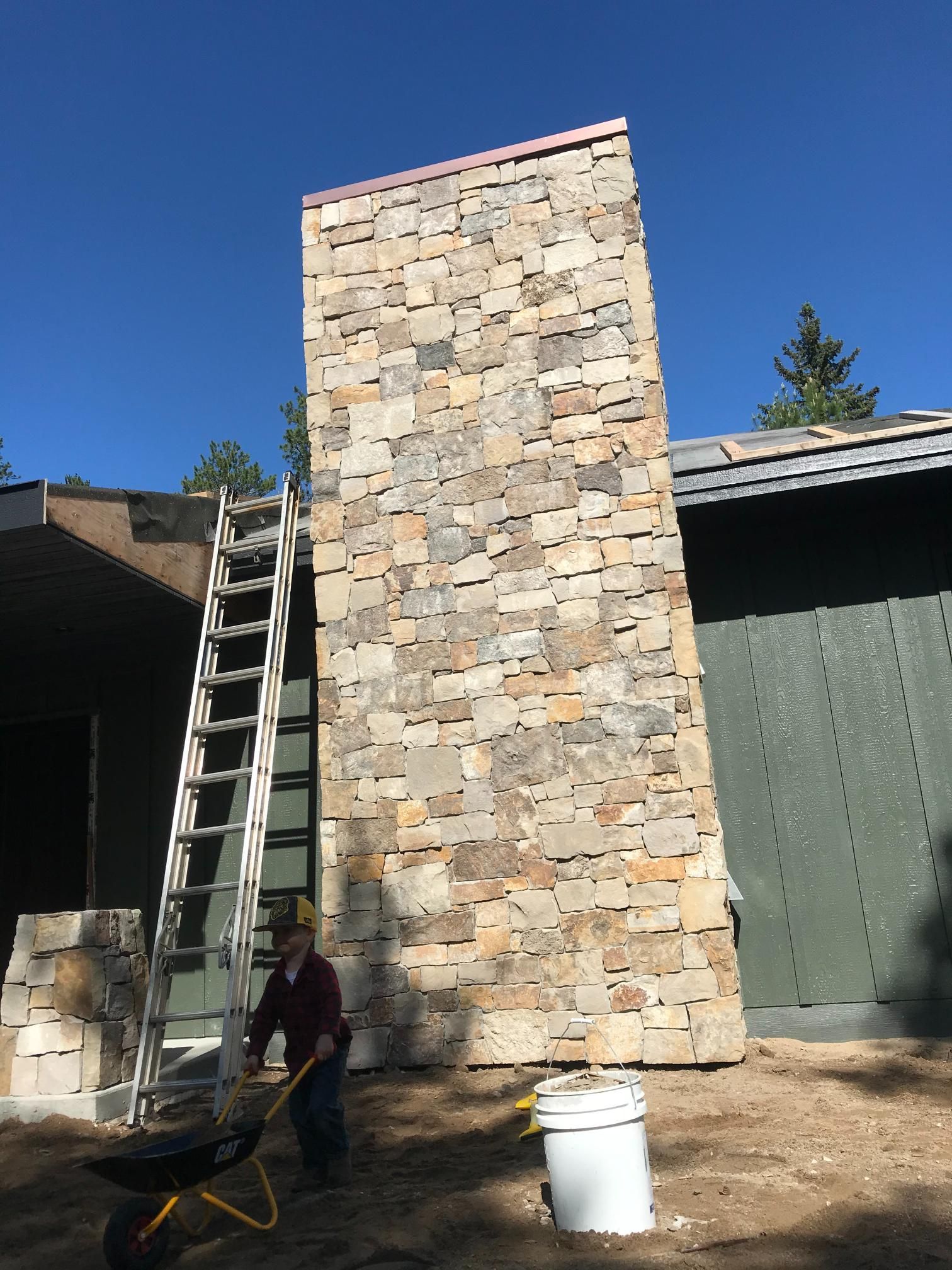 A man is standing in front of a large stone wall.