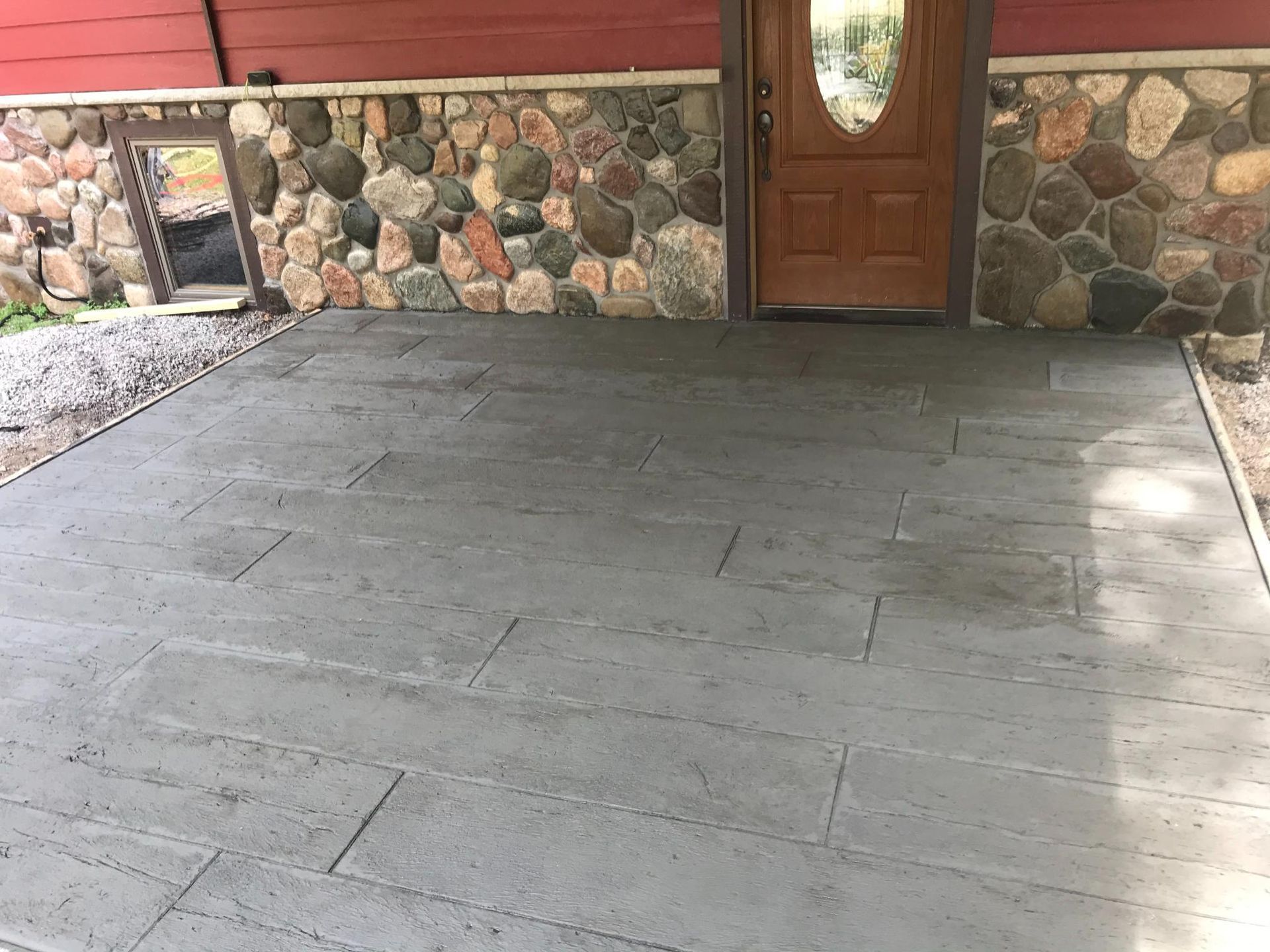 A concrete driveway in front of a house with a stone wall.