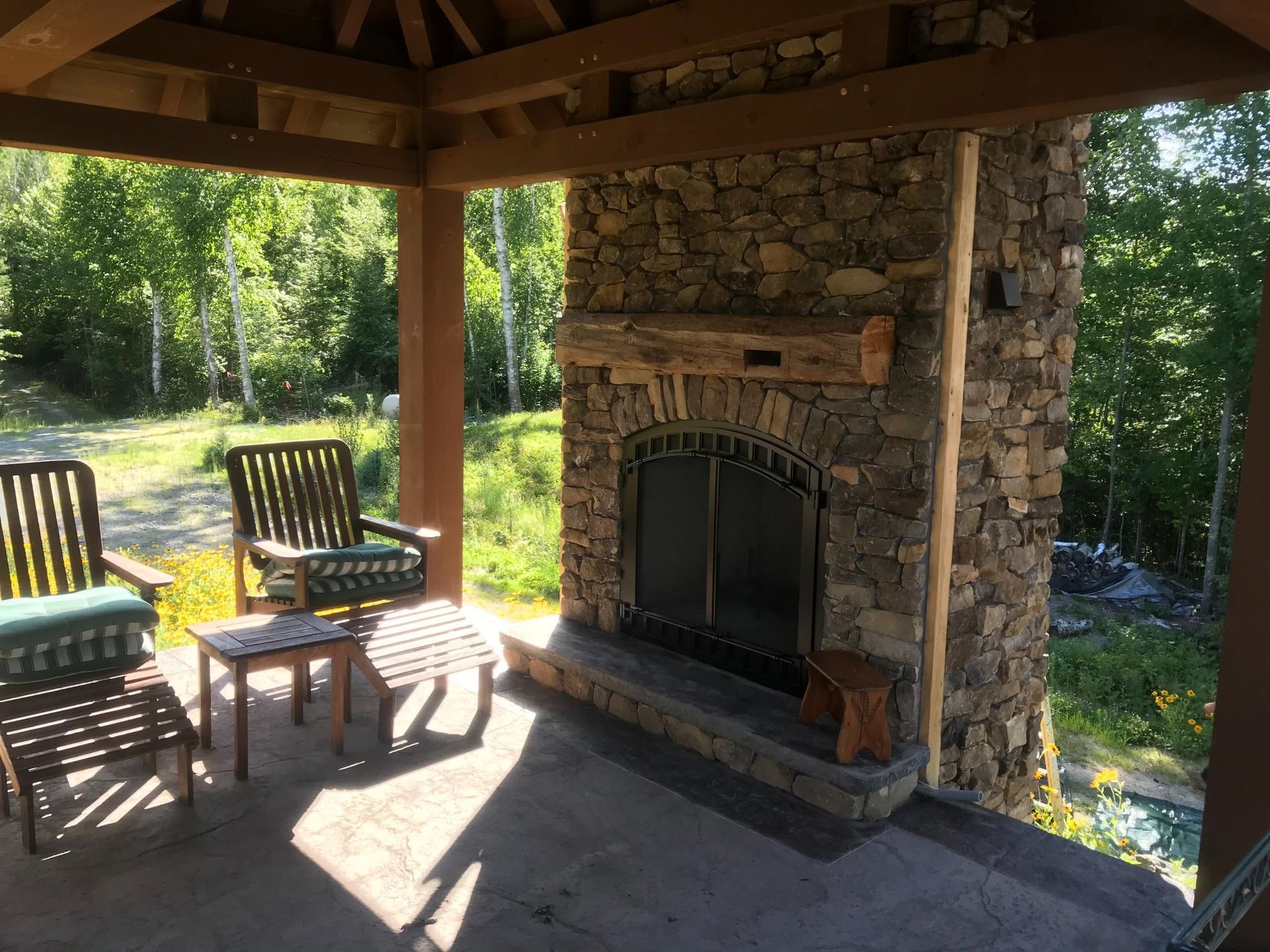 A stone fireplace under a gazebo with chairs and a table