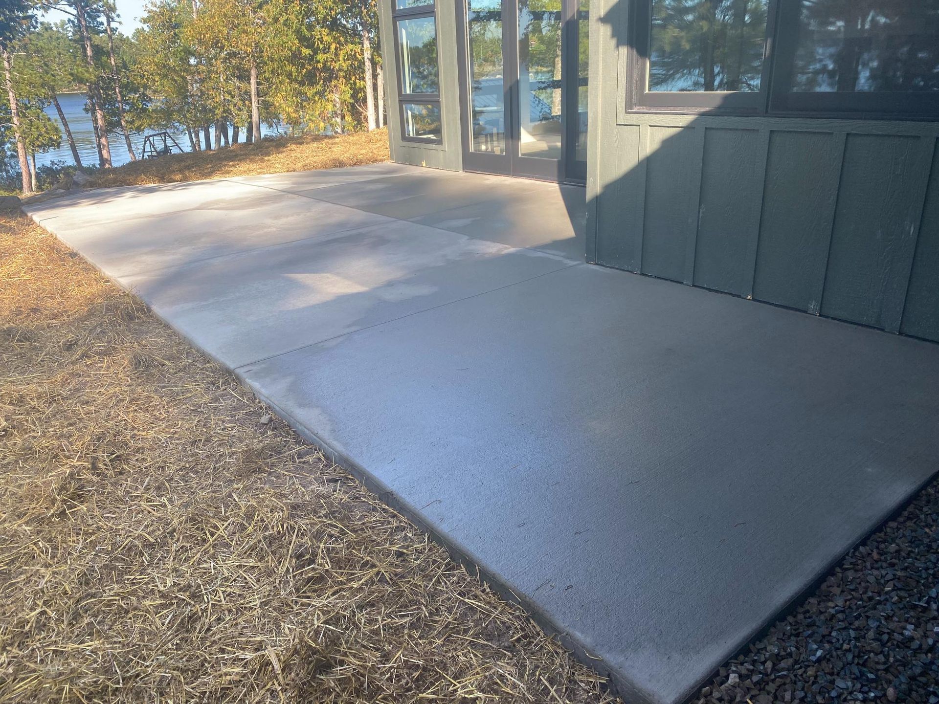 A concrete walkway leading to a house with a lake in the background.