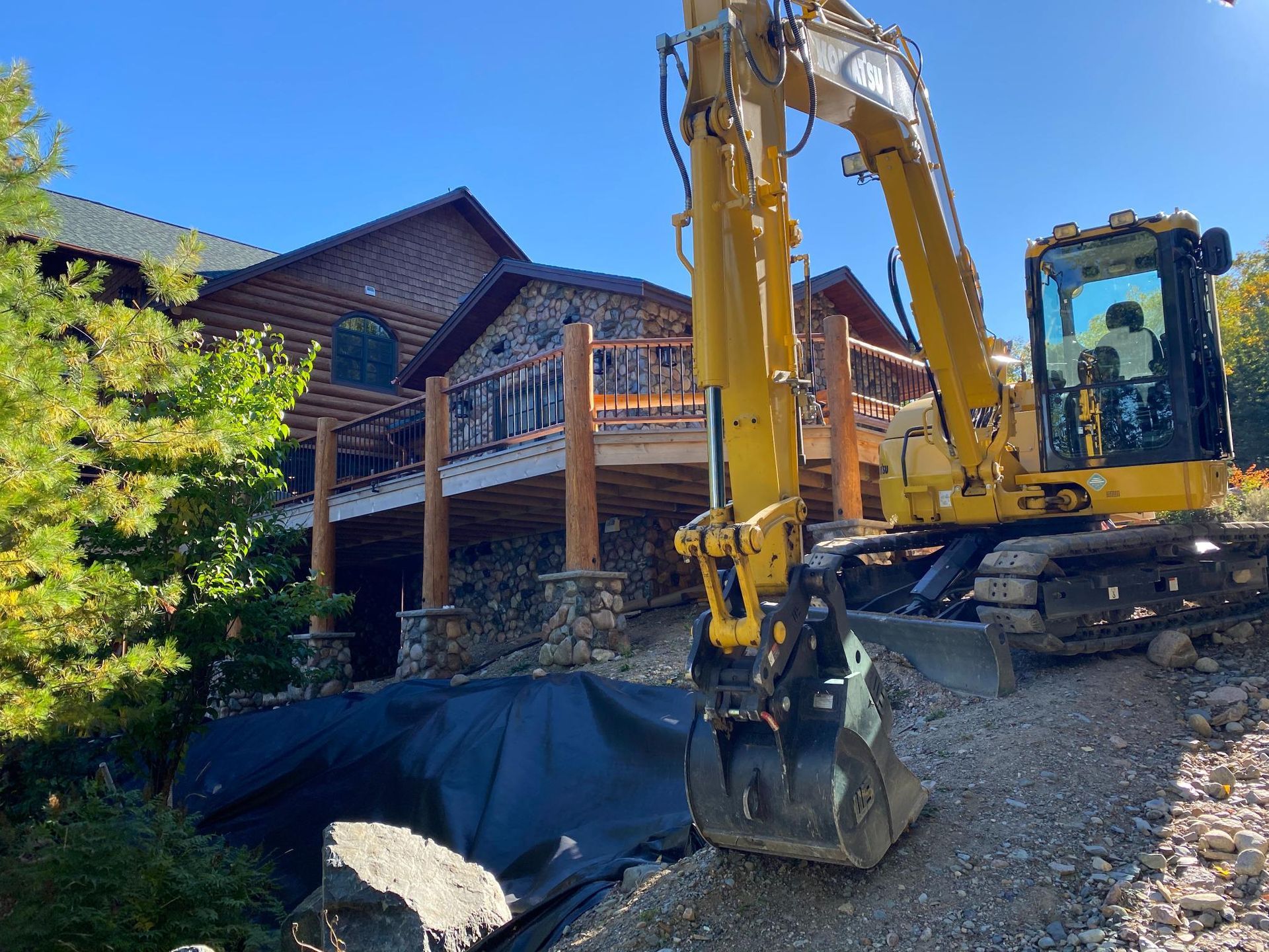 A large yellow excavator is sitting in front of a large house.