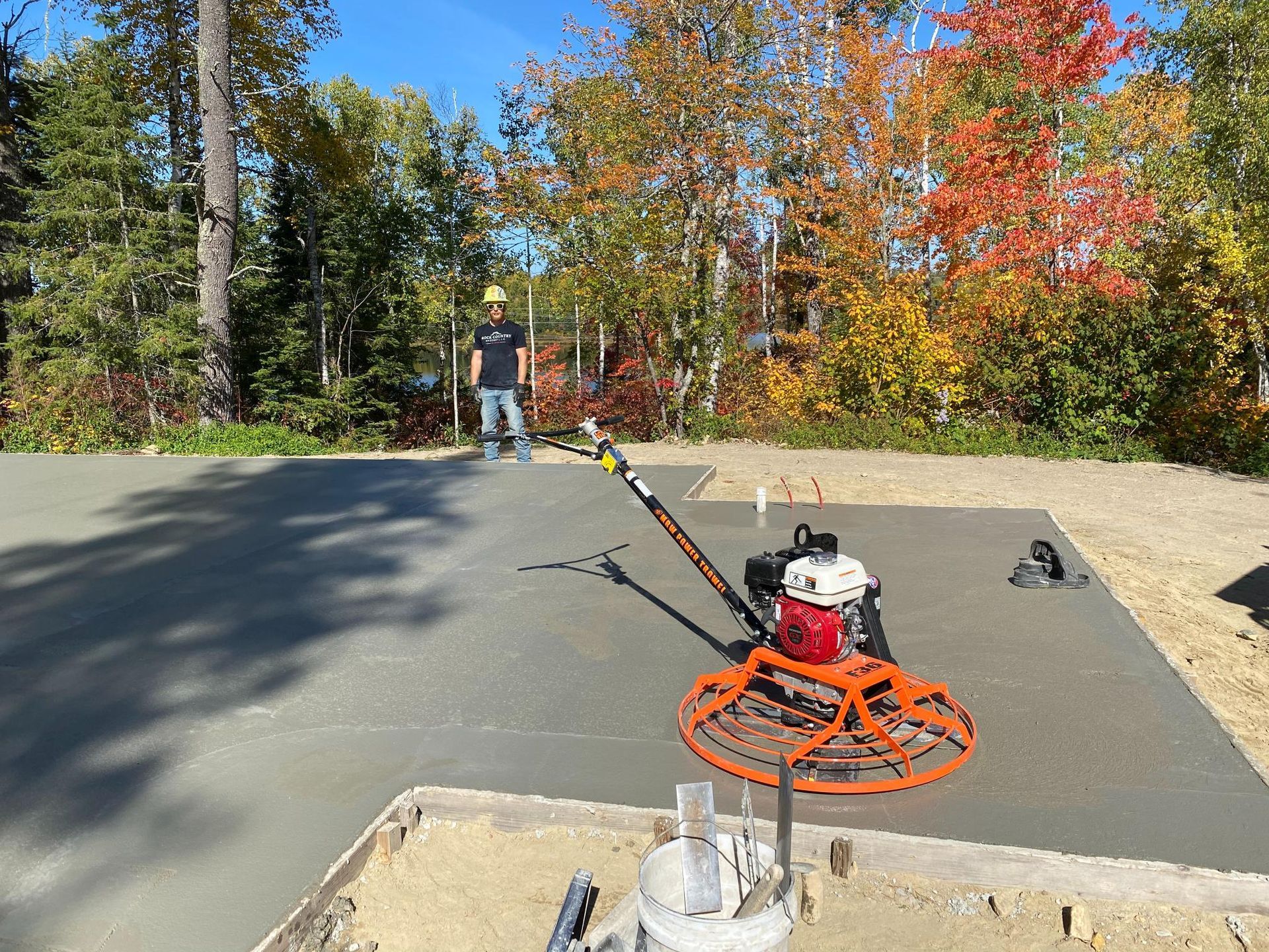 A man is standing next to a machine that is laying concrete.