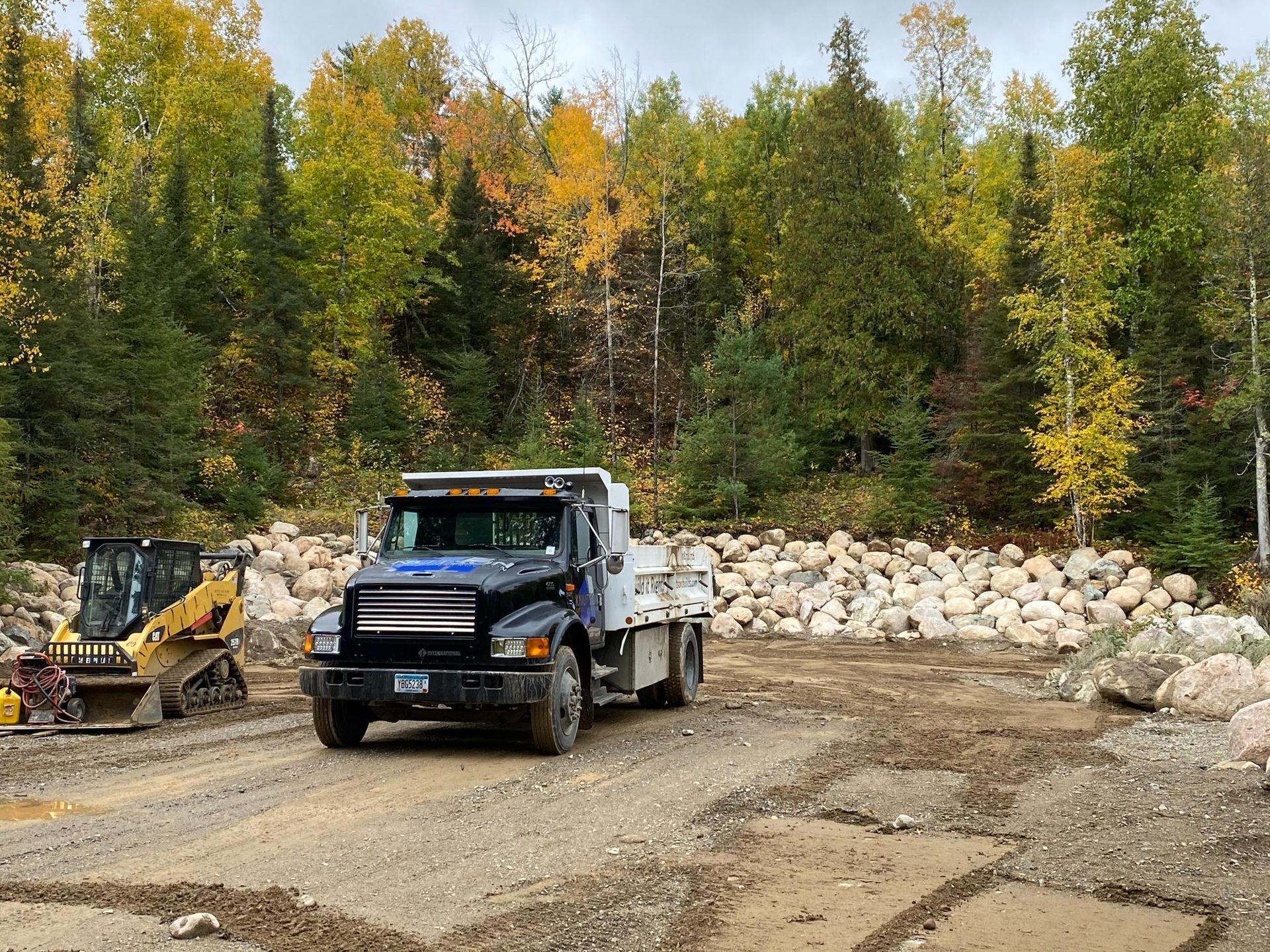 A dump truck is driving down a dirt road next to a bulldozer.