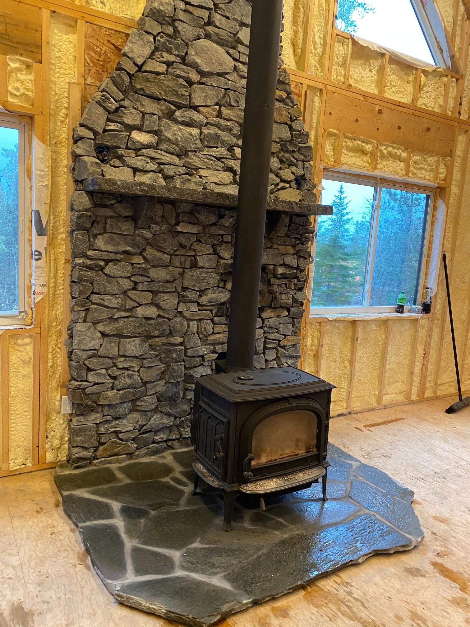 A wood stove is sitting in front of a stone fireplace in a room.