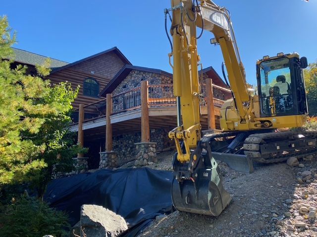 A large yellow excavator is sitting in front of a large house.