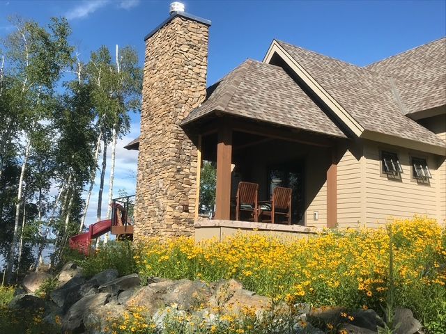 A house with a stone chimney is surrounded by yellow flowers.