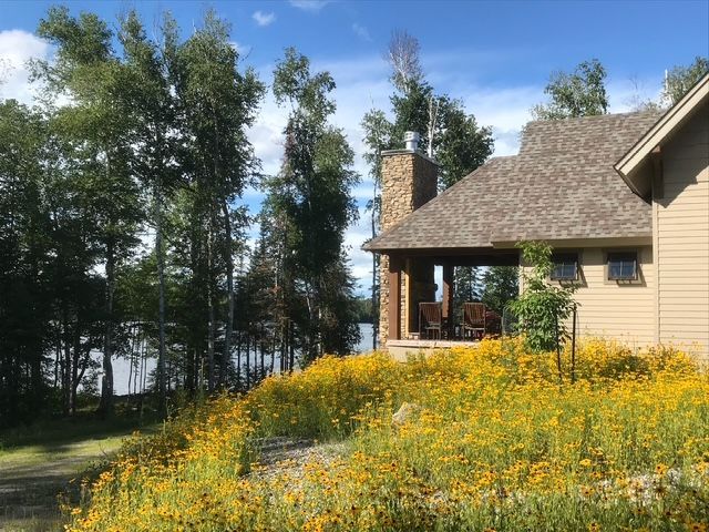 A house with a porch and a lot of yellow flowers in front of it.