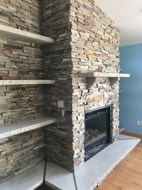 A living room with a stone fireplace and shelves