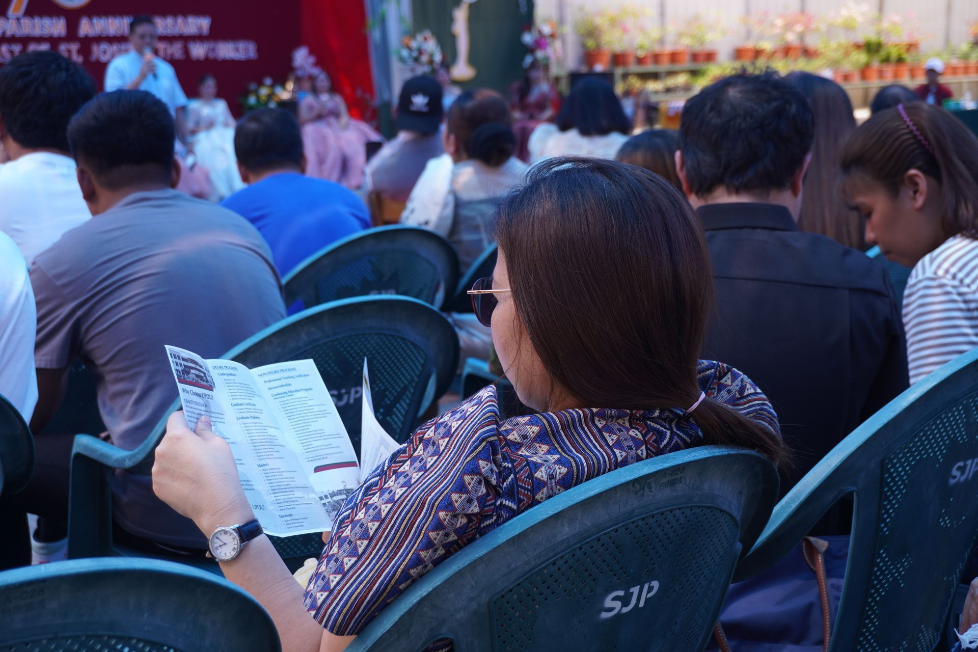 Person watering green plants with a hose outdoors on a sunny day.