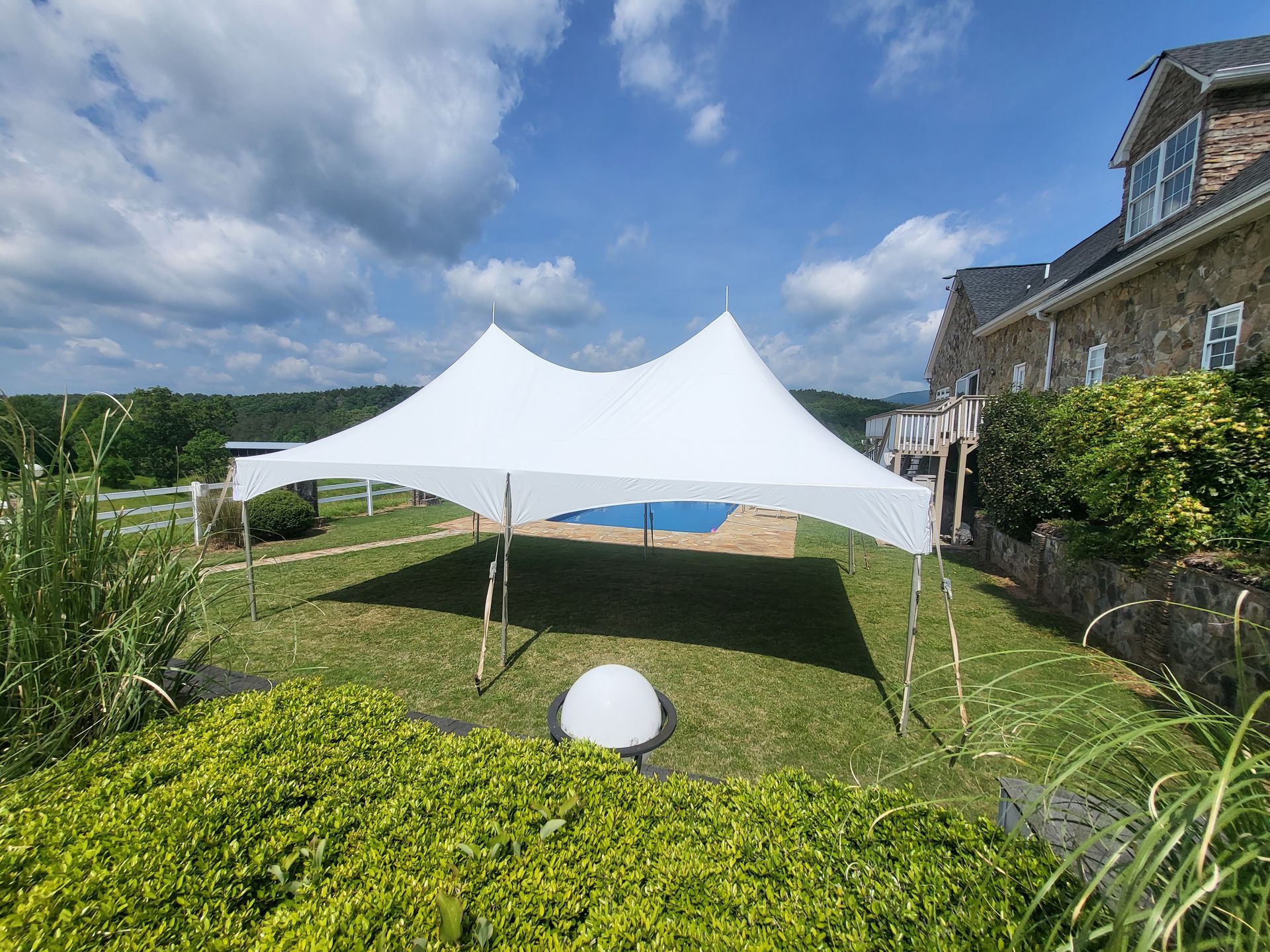 A white tent is sitting in the grass in front of a house.
