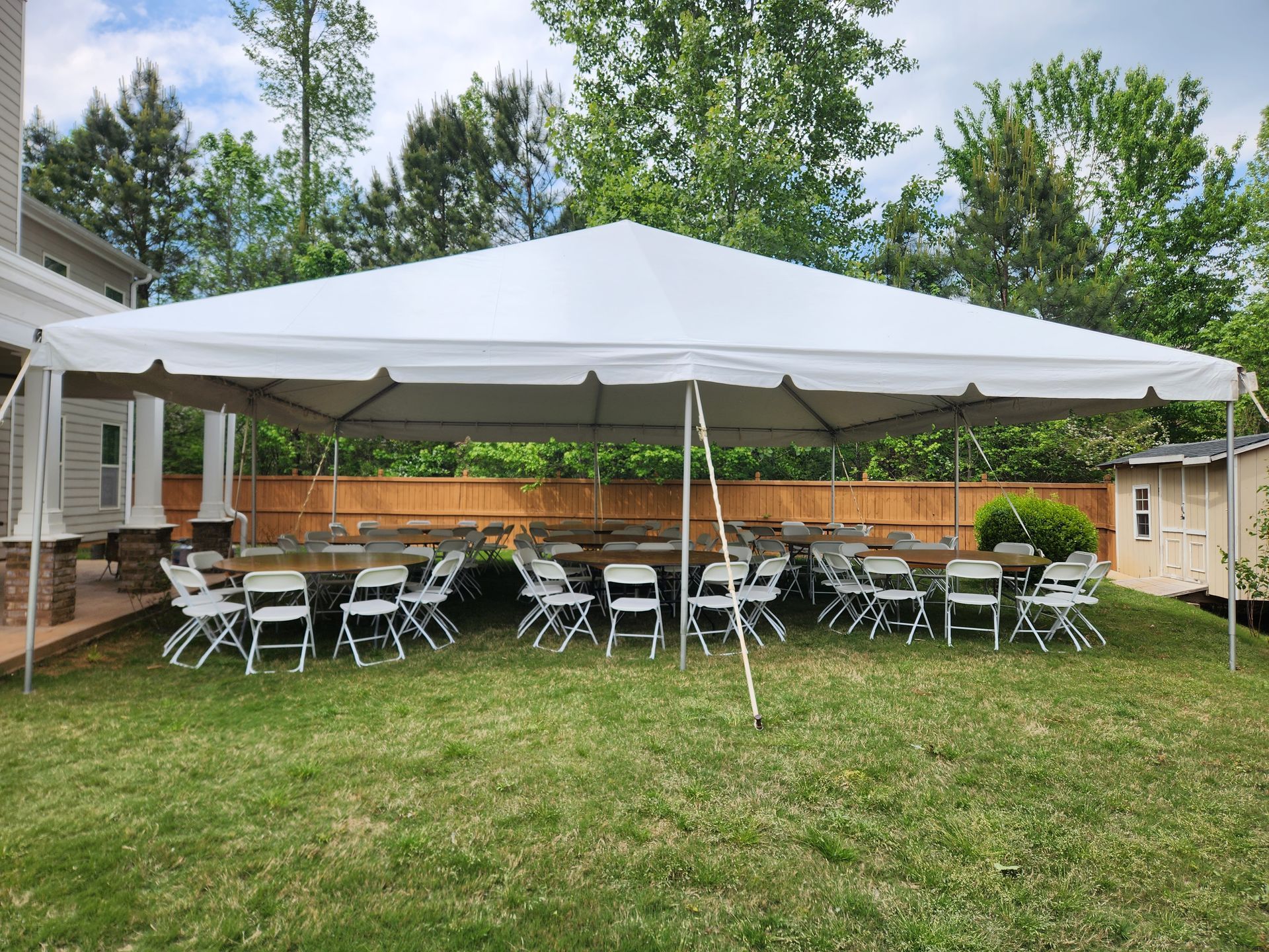 A large white tent with tables and chairs underneath it in a backyard.