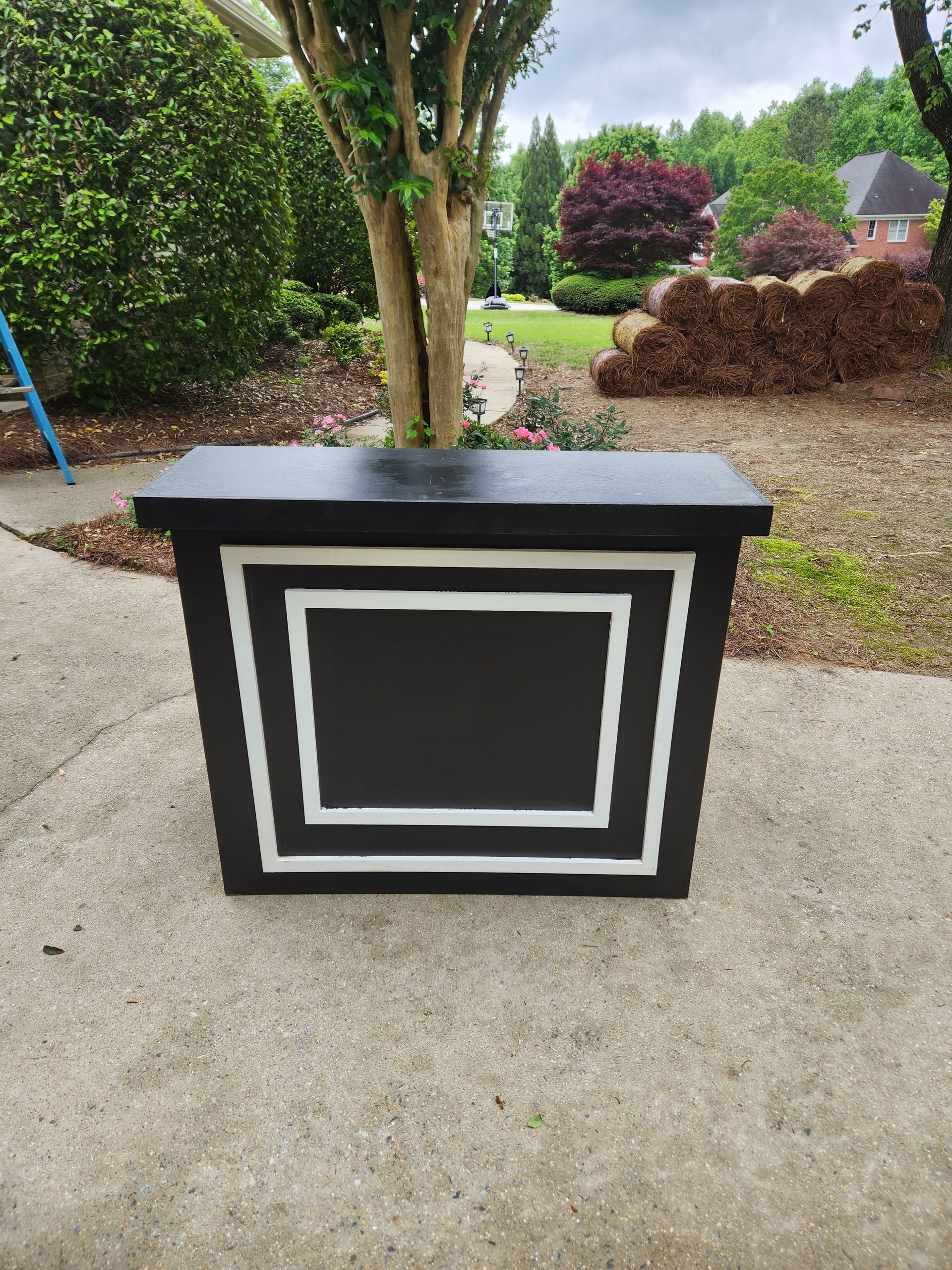 A black and white box is sitting on a sidewalk next to a tree.