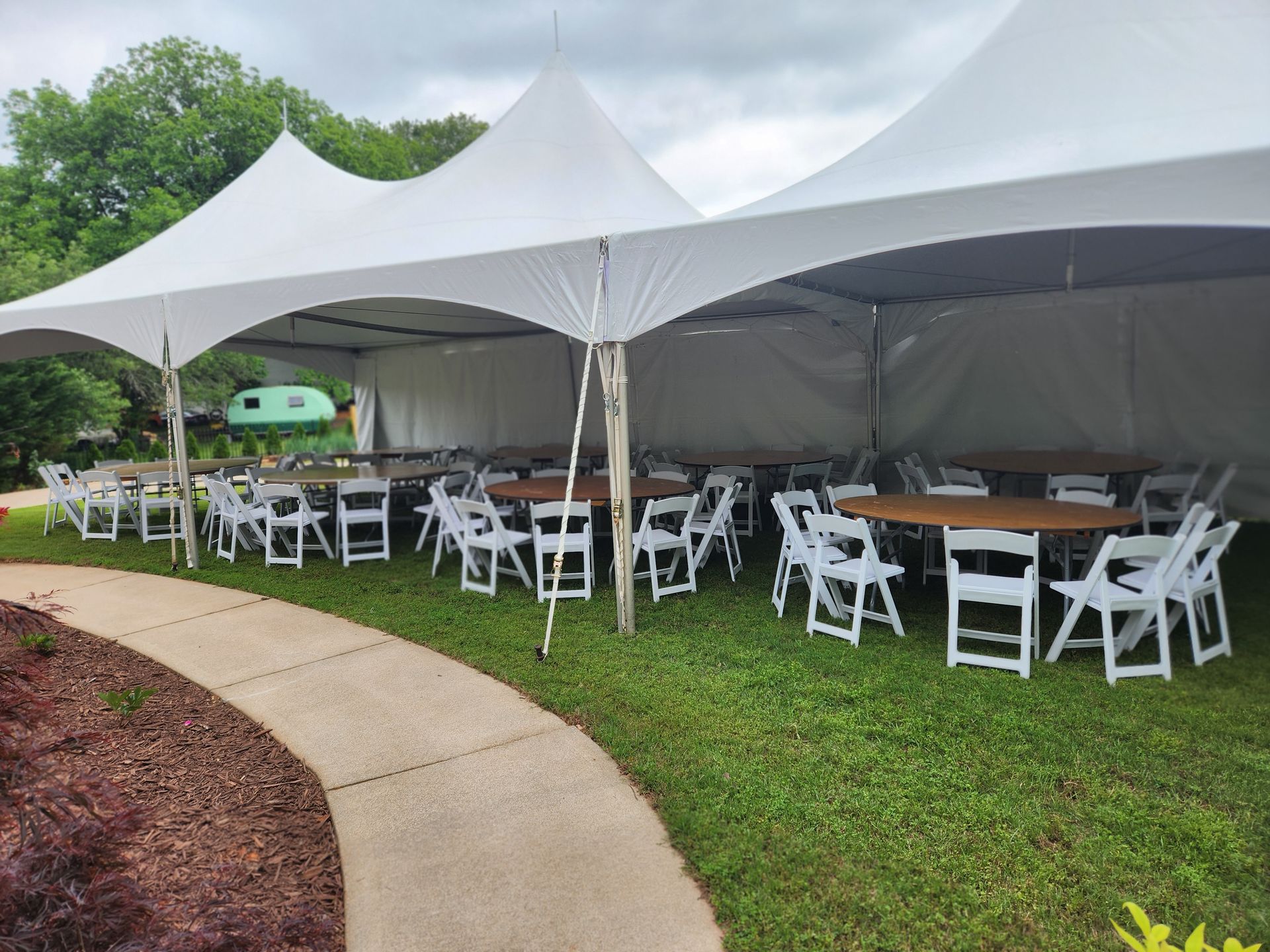 A row of white chairs and tables under a tent.