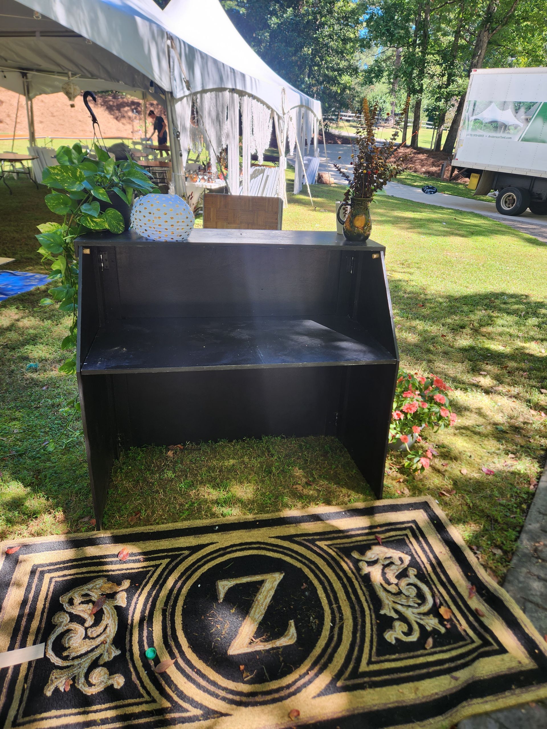 A black bench is sitting in the grass next to a rug with the letter z on it.